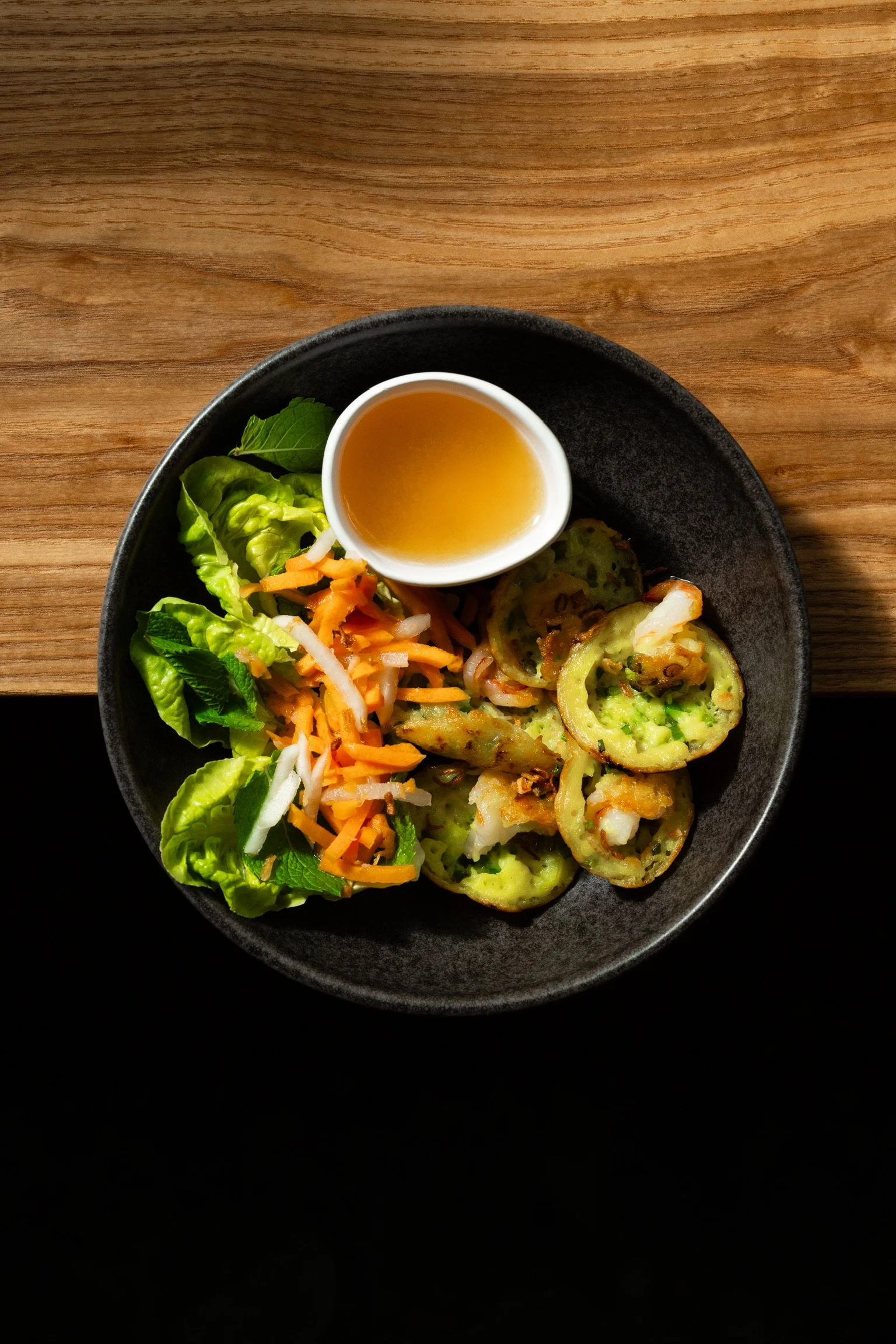Assiette de légumes frits avec une sauce dans un petit bol, garnie de salade verte, carottes râpées, et autres légumes.