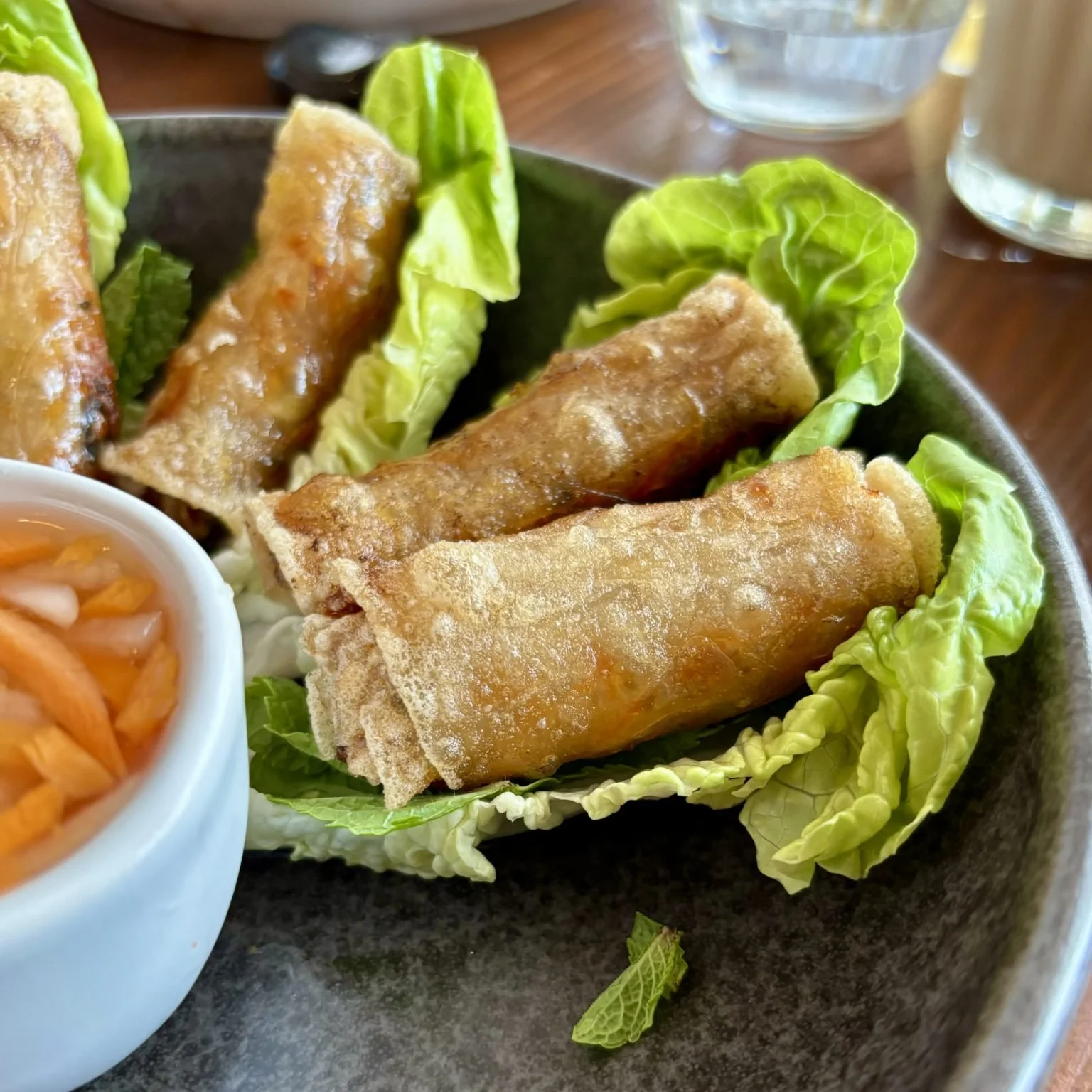 Rouleaux de printemps frits servis sur des feuilles de laitue avec un petit bol de sauce.