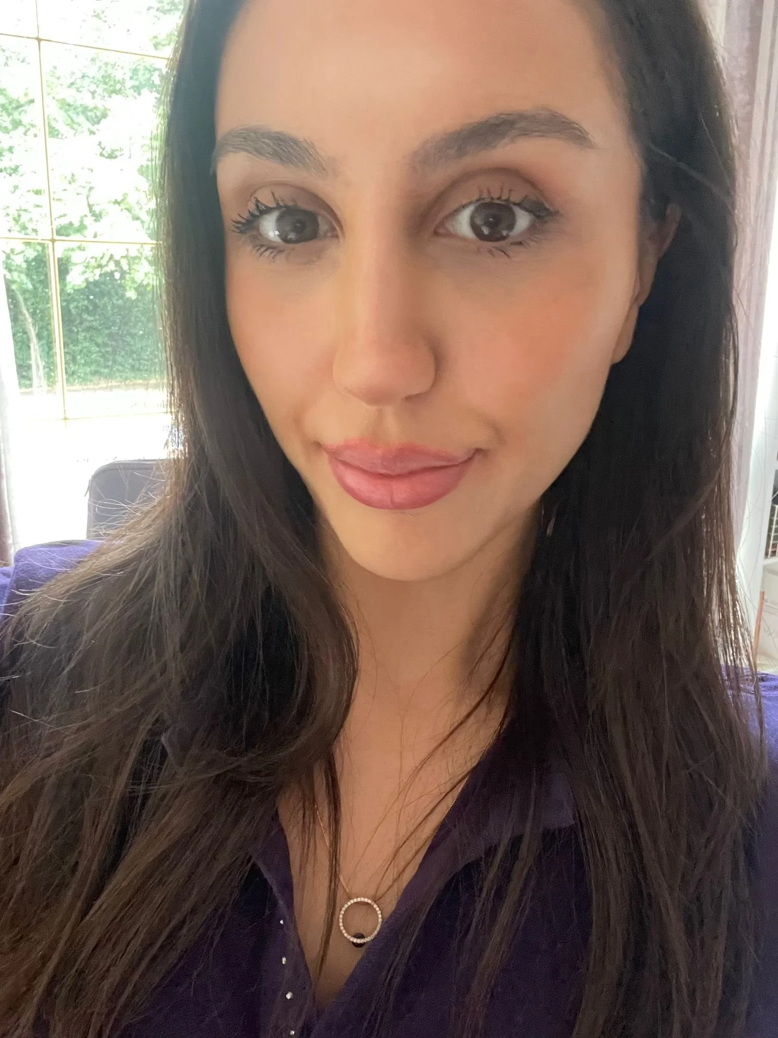 A young woman with long brown hair smiling at the camera, with a purple and blue gradient background.