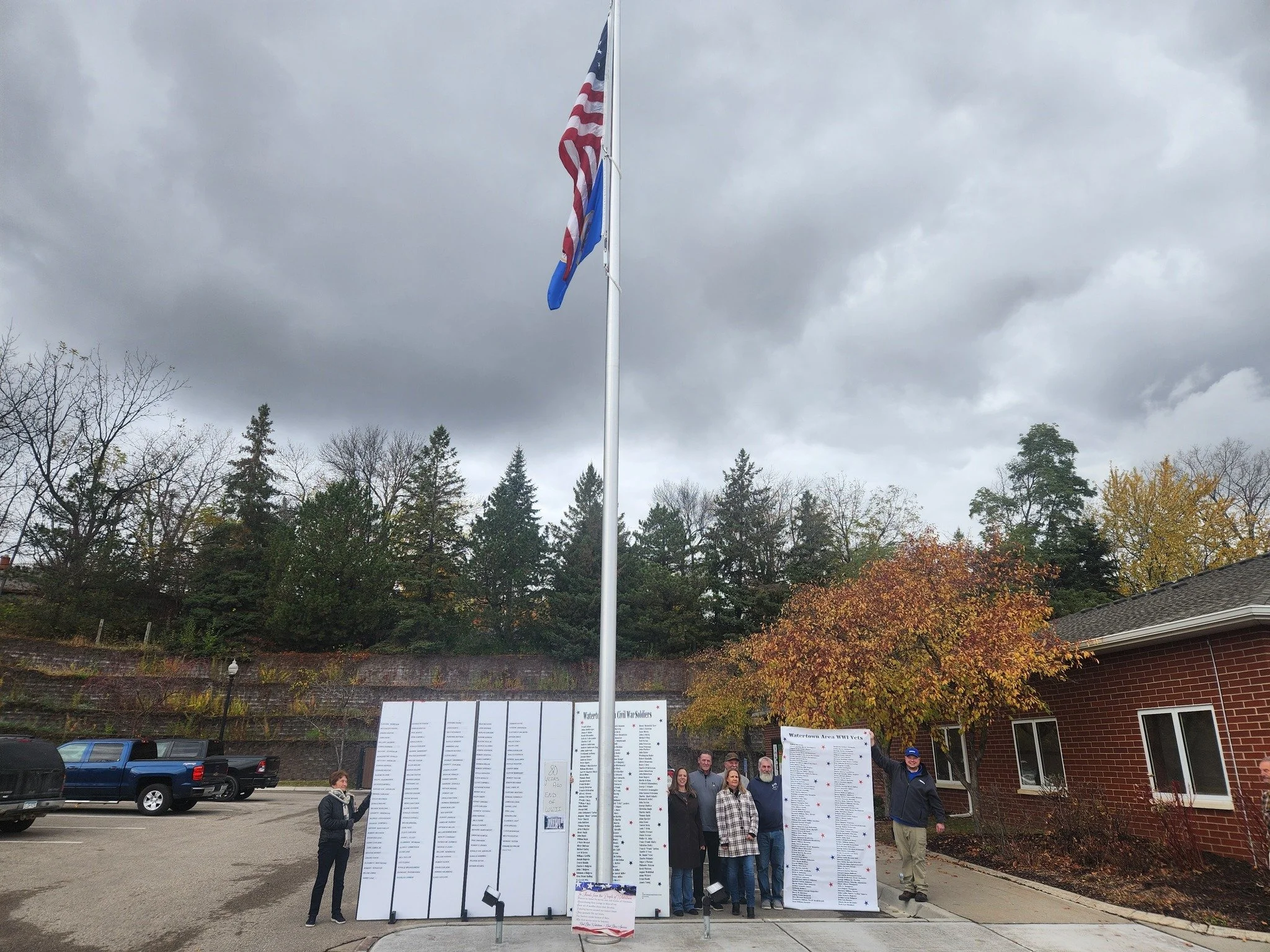 The Ceremony honoring the installation of the new  flag pole at the Watertown City Hall with Watertown dignitaries and signs listing veterans from Watertown that have given their lives in service.