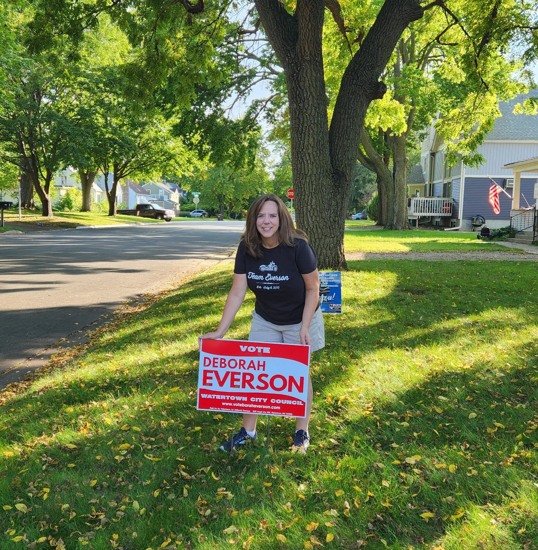 Deborah Everson is in a yard placing a yard sign for her campaign.