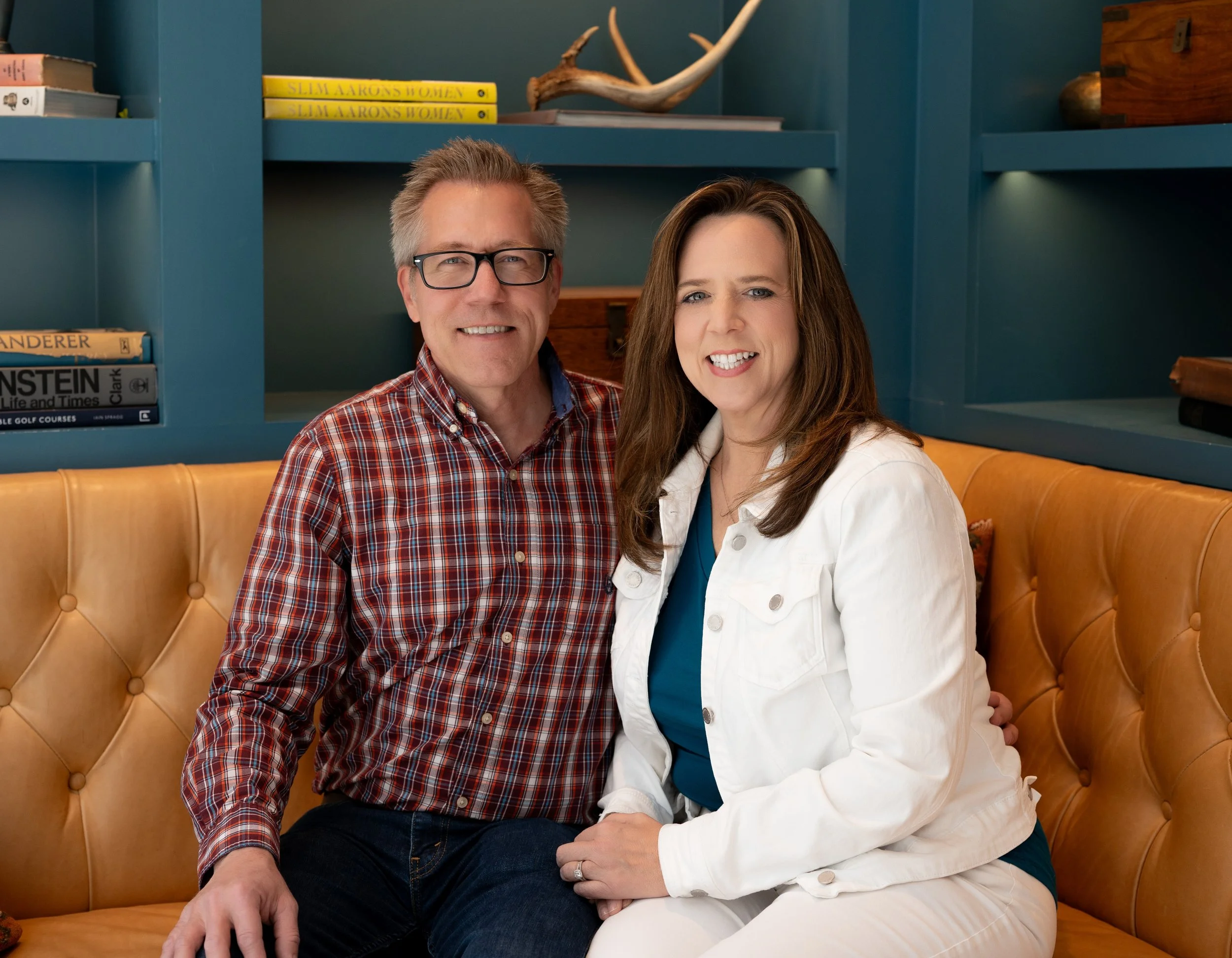 Deborah Everson and her husband Tracy sitting on a tan leather couch in a library.