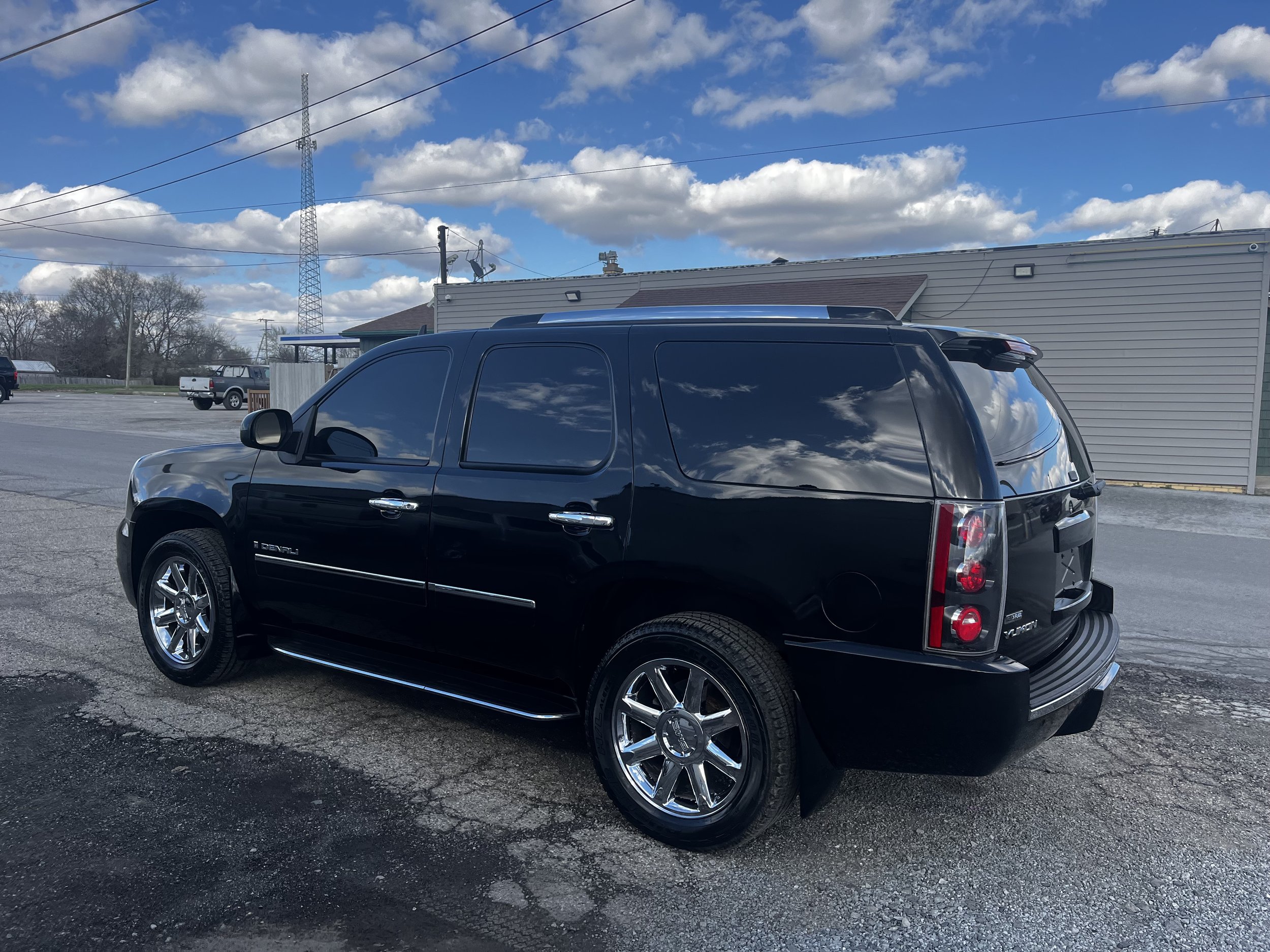 Black SUV parked near a building under a cloudy blue sky.