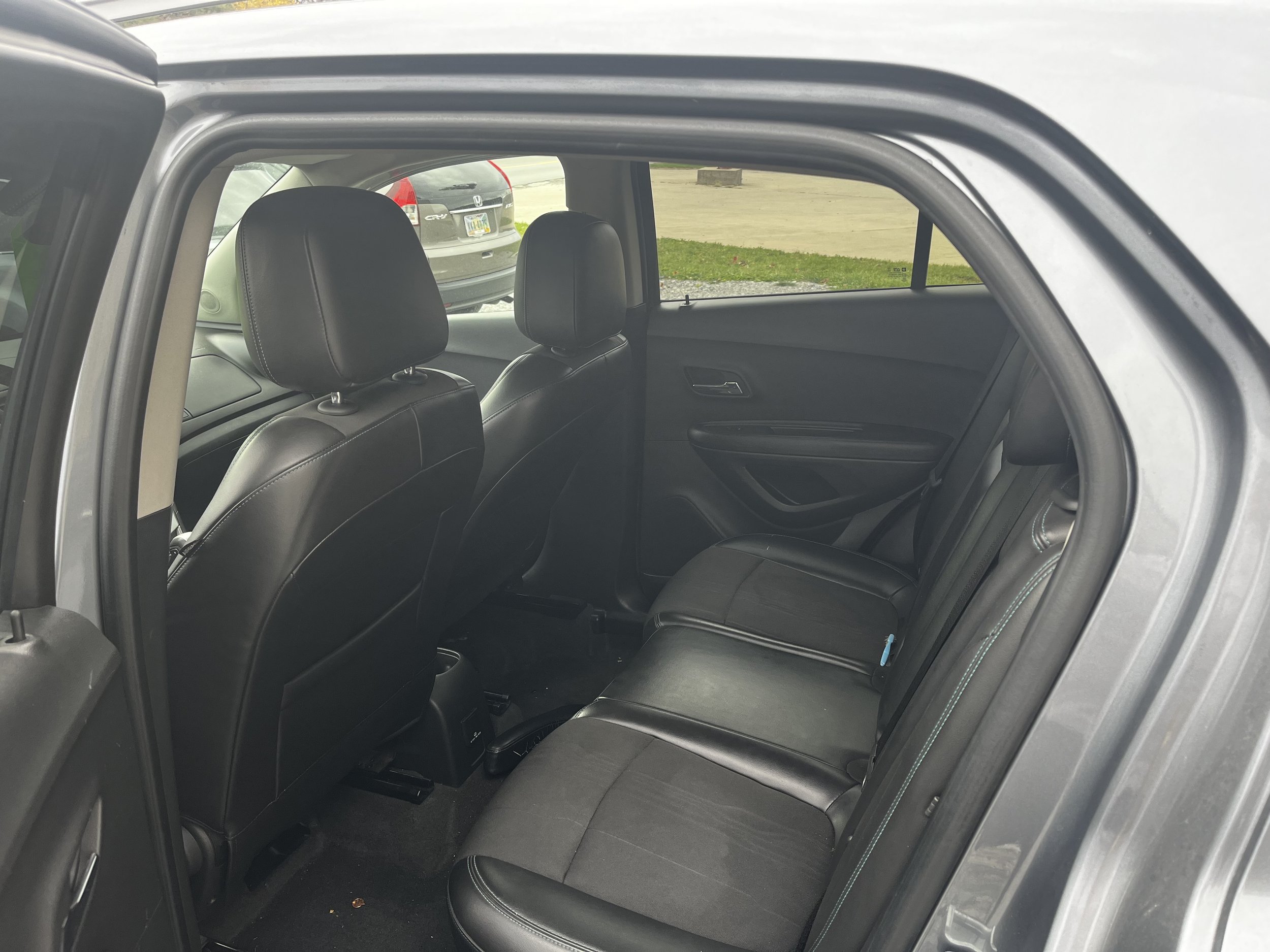 Interior of a car, focusing on the back seat with black leather upholstery and two front seats visible.