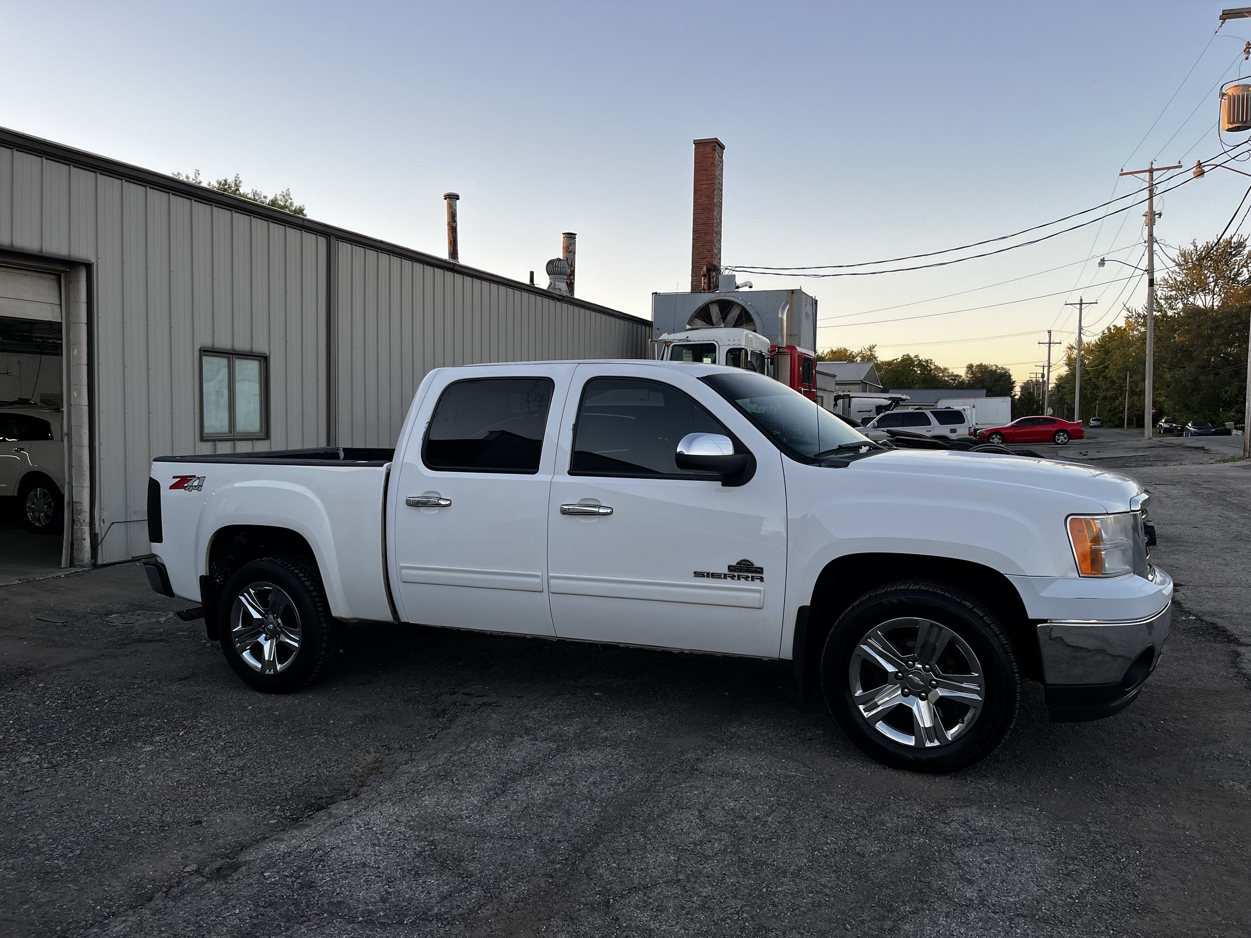 White pickup truck parked next to a metal building in an industrial area.
