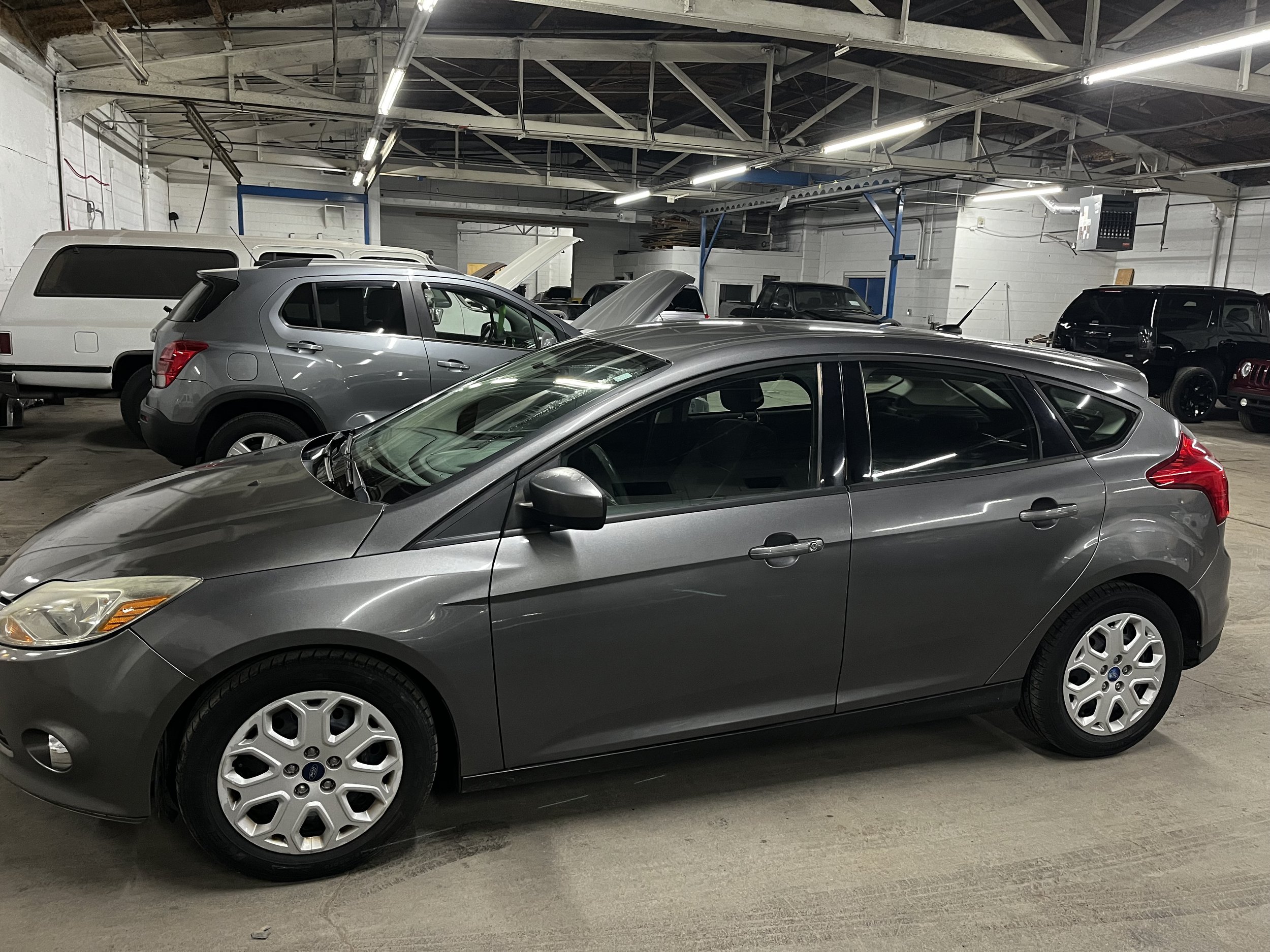 Gray hatchback car parked inside a garage with other vehicles in the background.