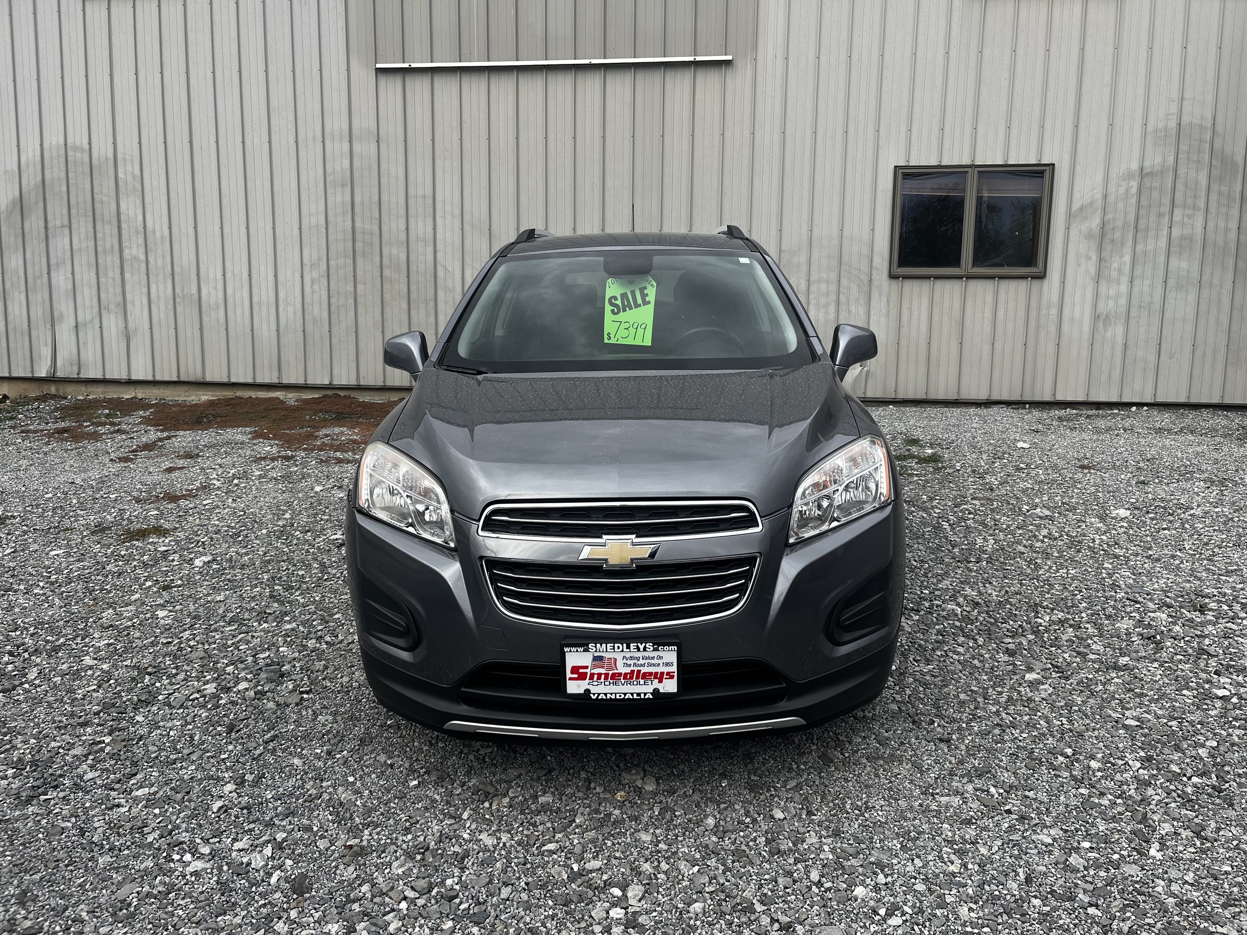 Front view of a gray Chevrolet SUV parked on gravel with a "For Sale" sign on the windshield, showing price $7,399.