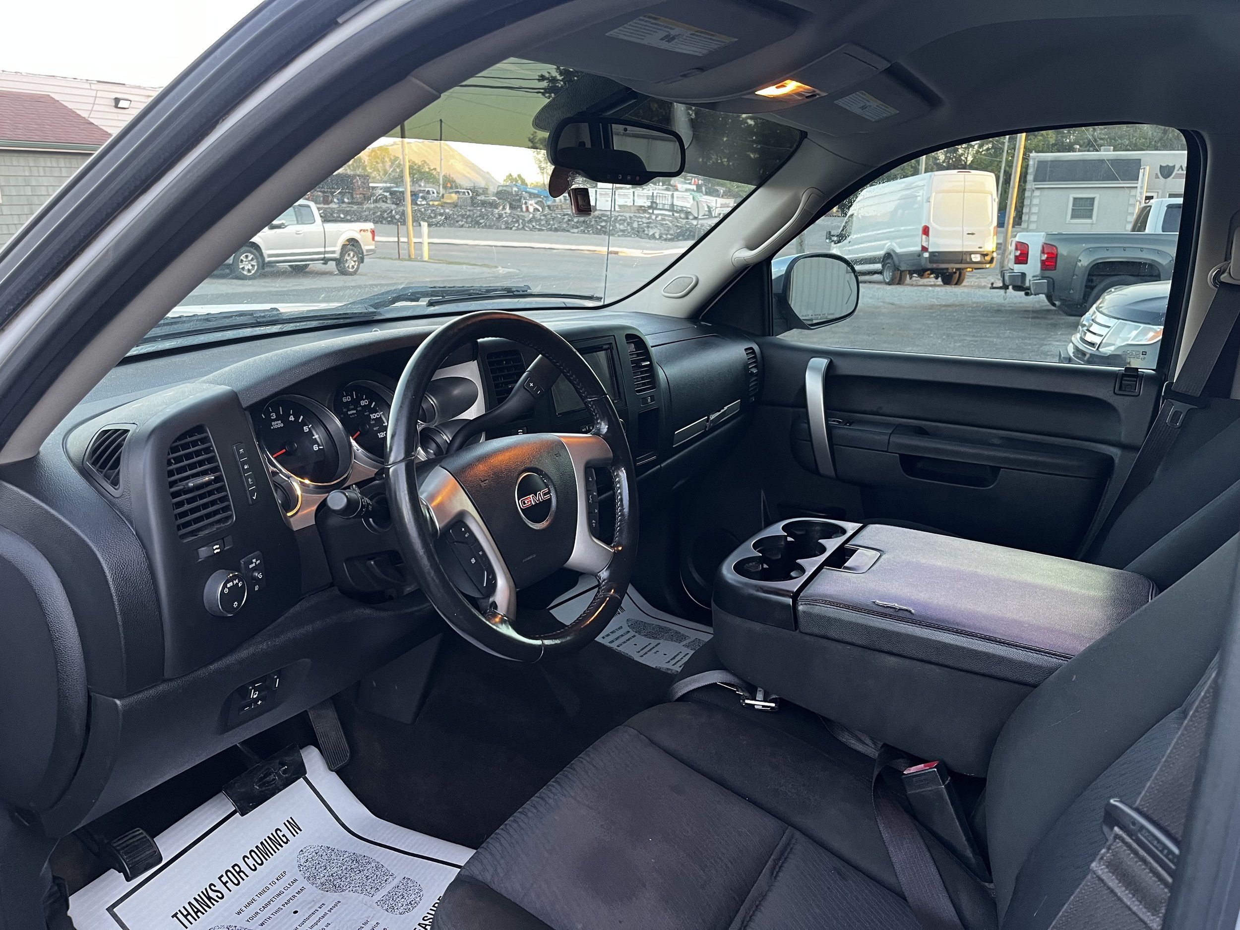 Interior of a GMC truck with steering wheel and front seats visible, featuring a central console with cup holders.