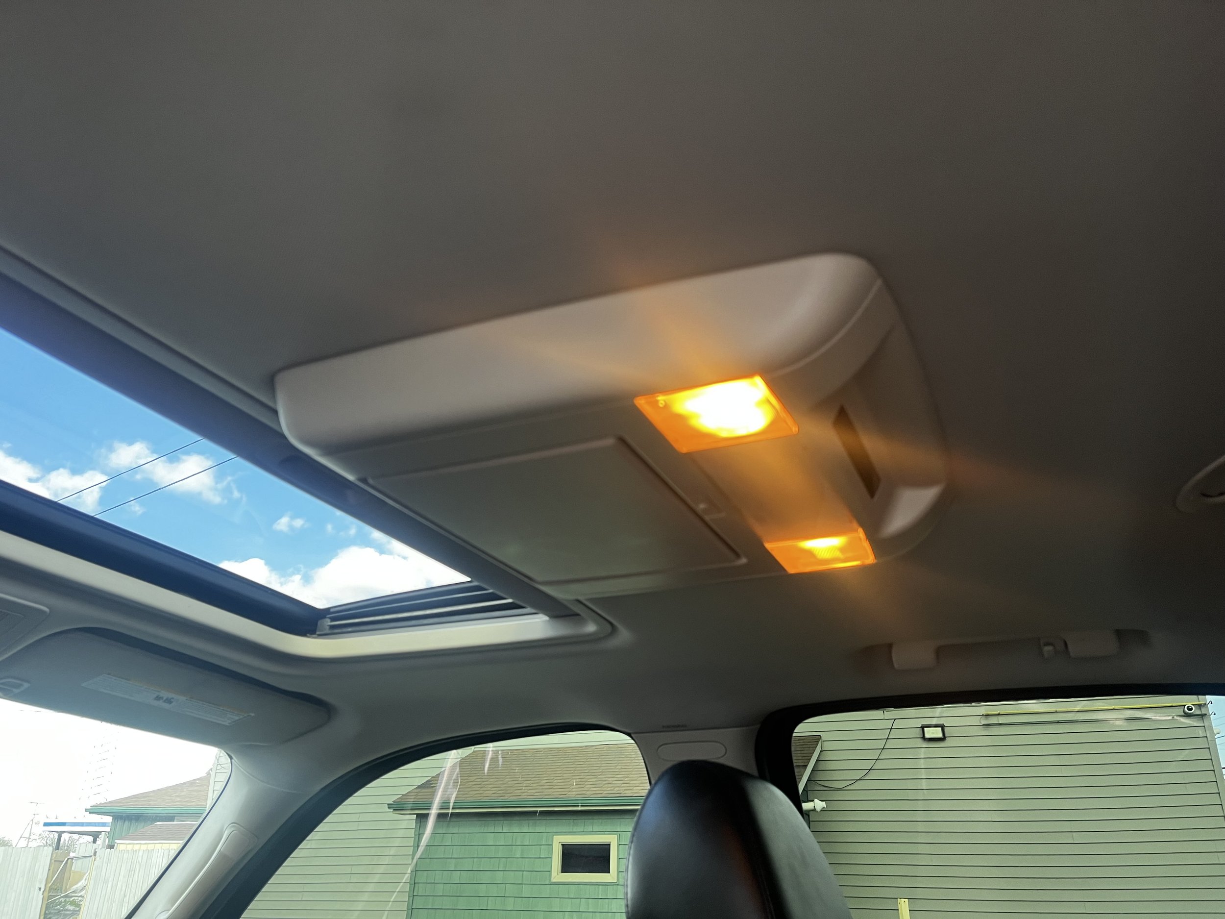 Sunroof view from inside a car with two interior lights on, showing a partially open sunroof and outdoor sky.