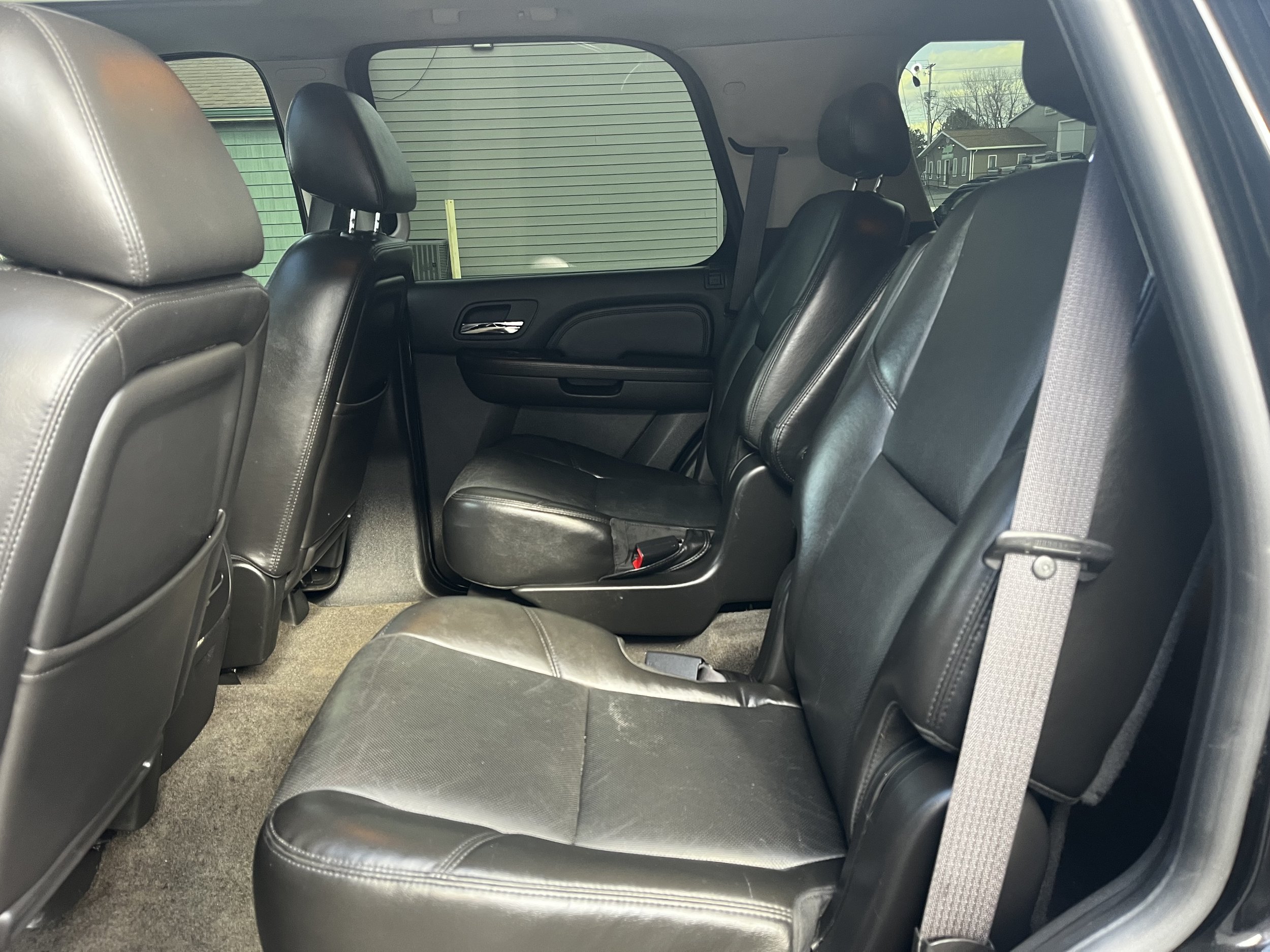 Interior of a vehicle with black leather seats and a door partially open, showing the second row seating area.