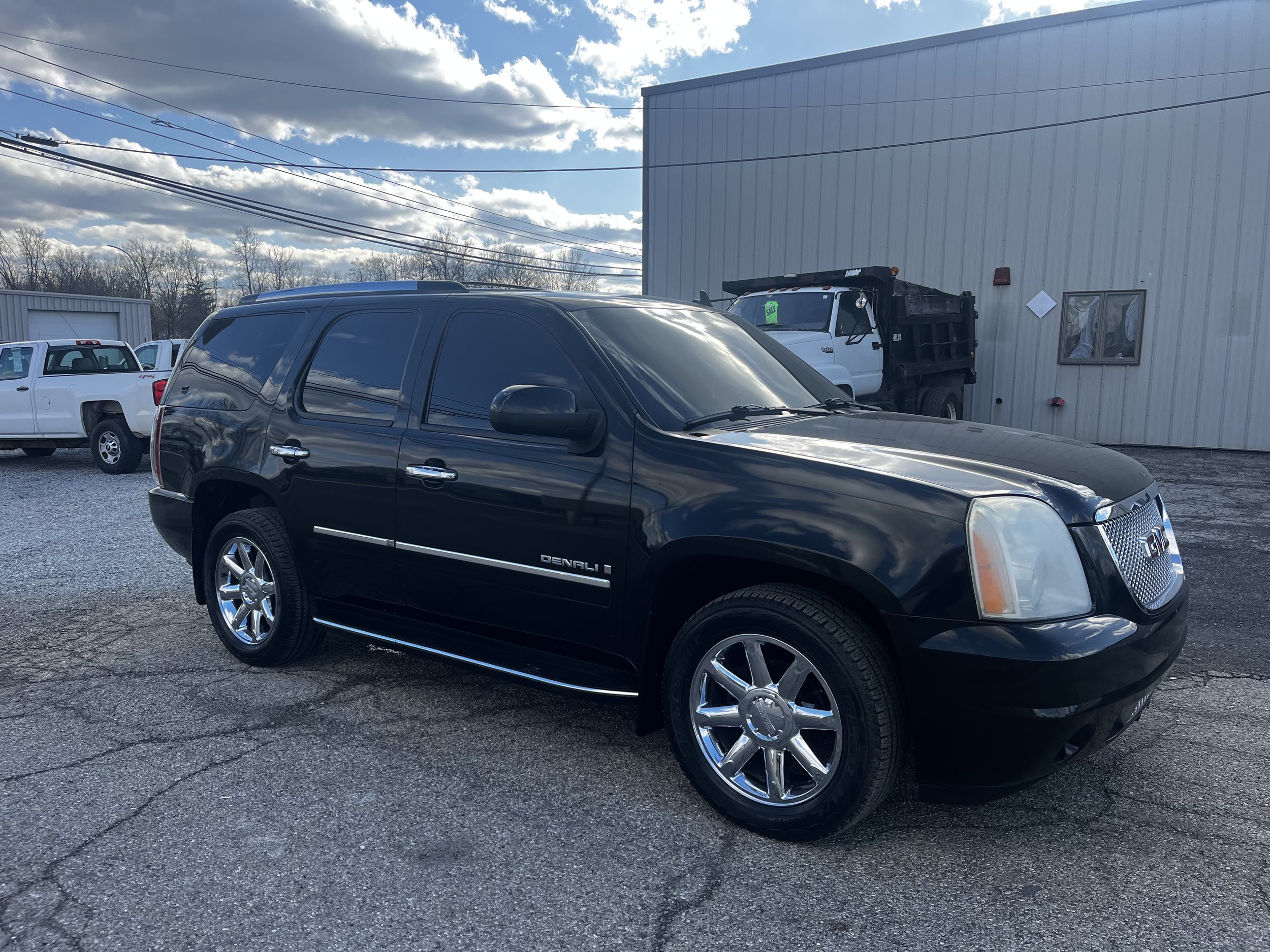 Black GMC Denali SUV parked on a paved lot, with a building in the background and other vehicles nearby.