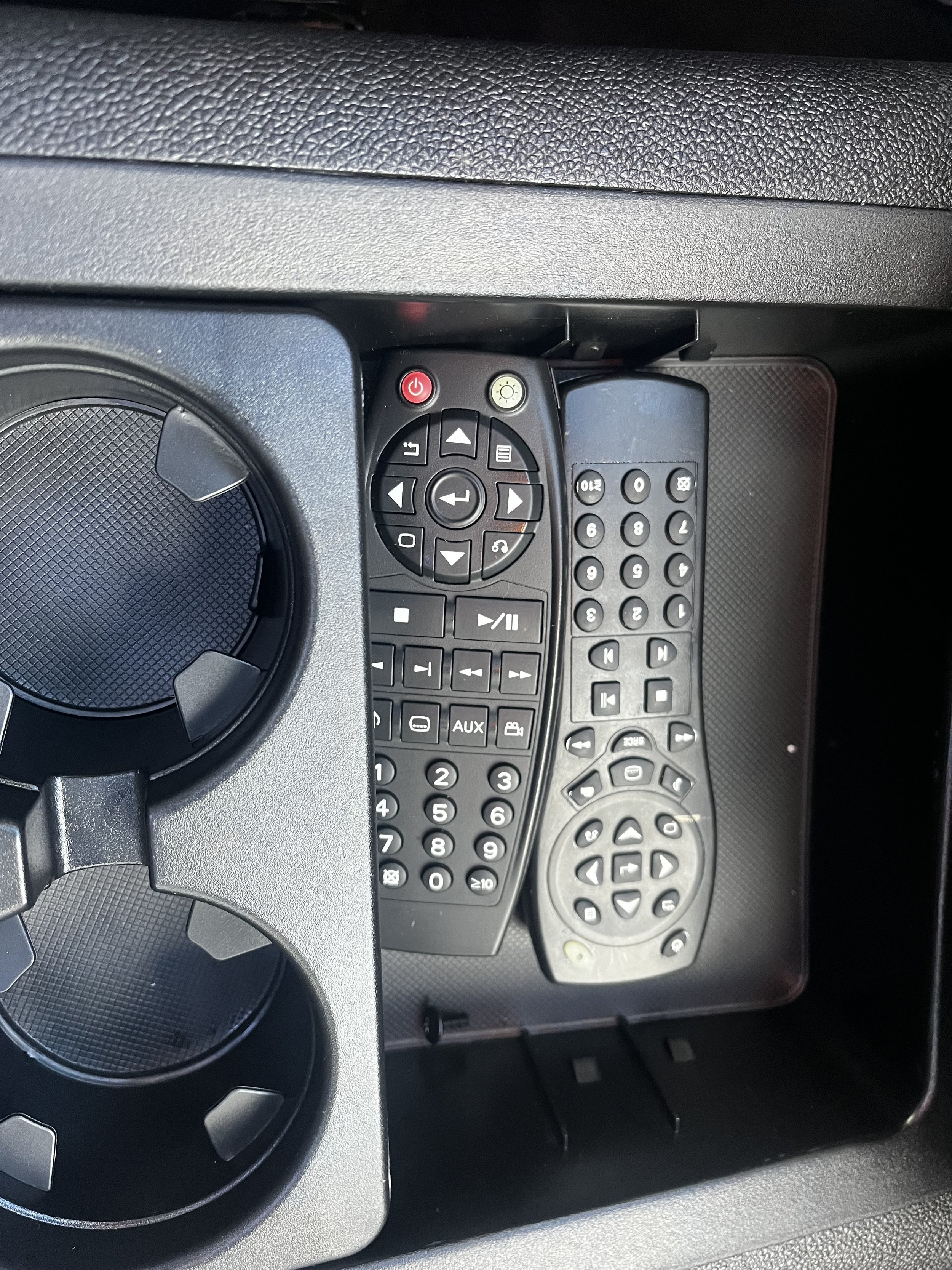 Two remote controls in a vehicle's center console compartment next to cup holders.