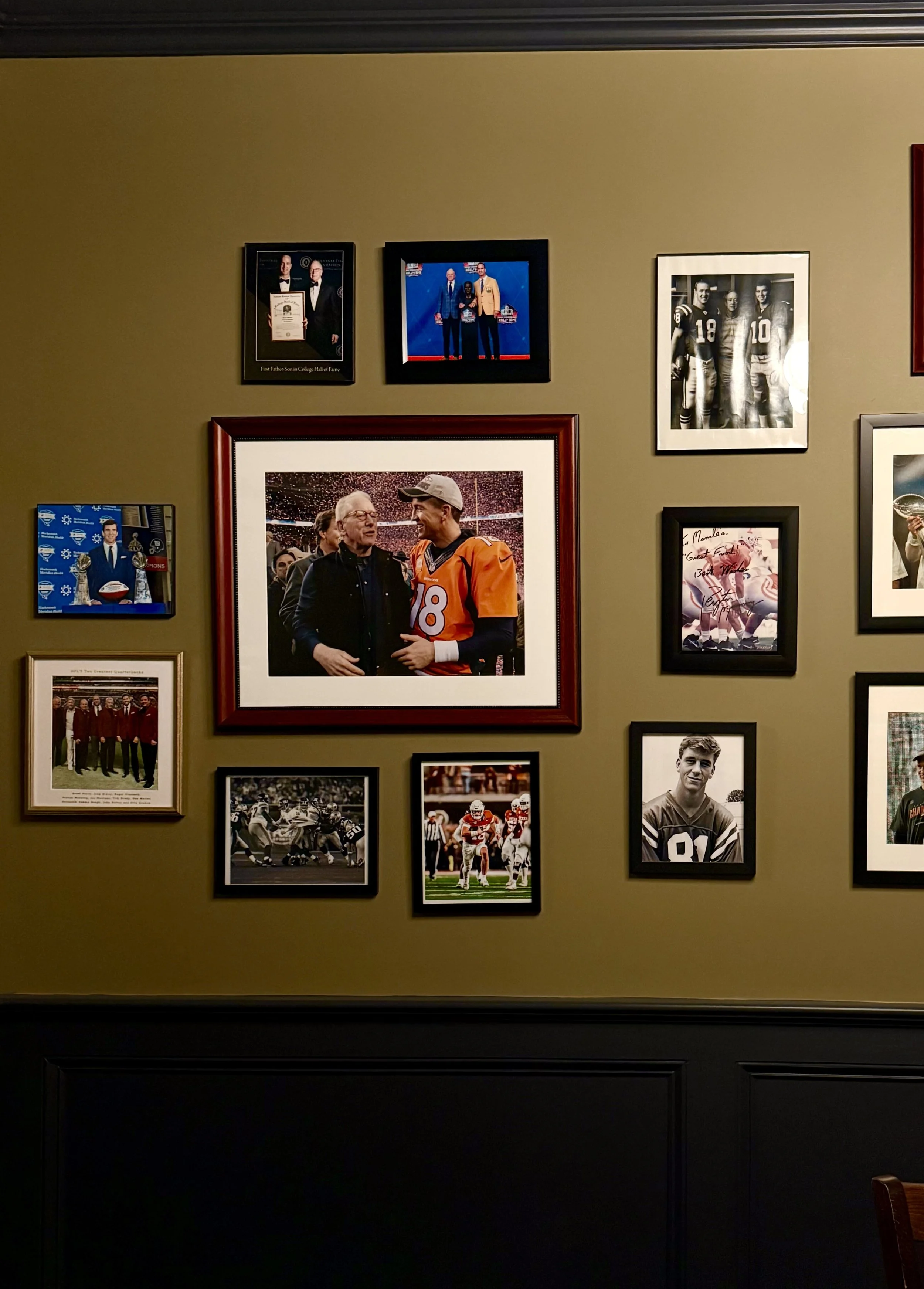 Wall with framed photographs and sports memorabilia, including a photo of a football player, a picture of football players in a team huddle, and images of athletes and award ceremonies.