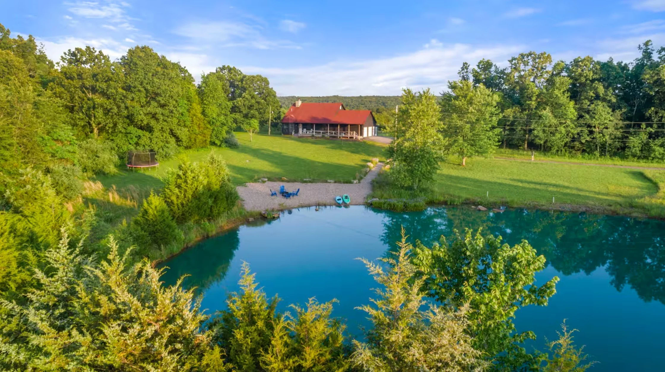 A scenic view of a lakeside property with a house, lush green trees, and a grassy lawn, captured during daytime with clear skies.