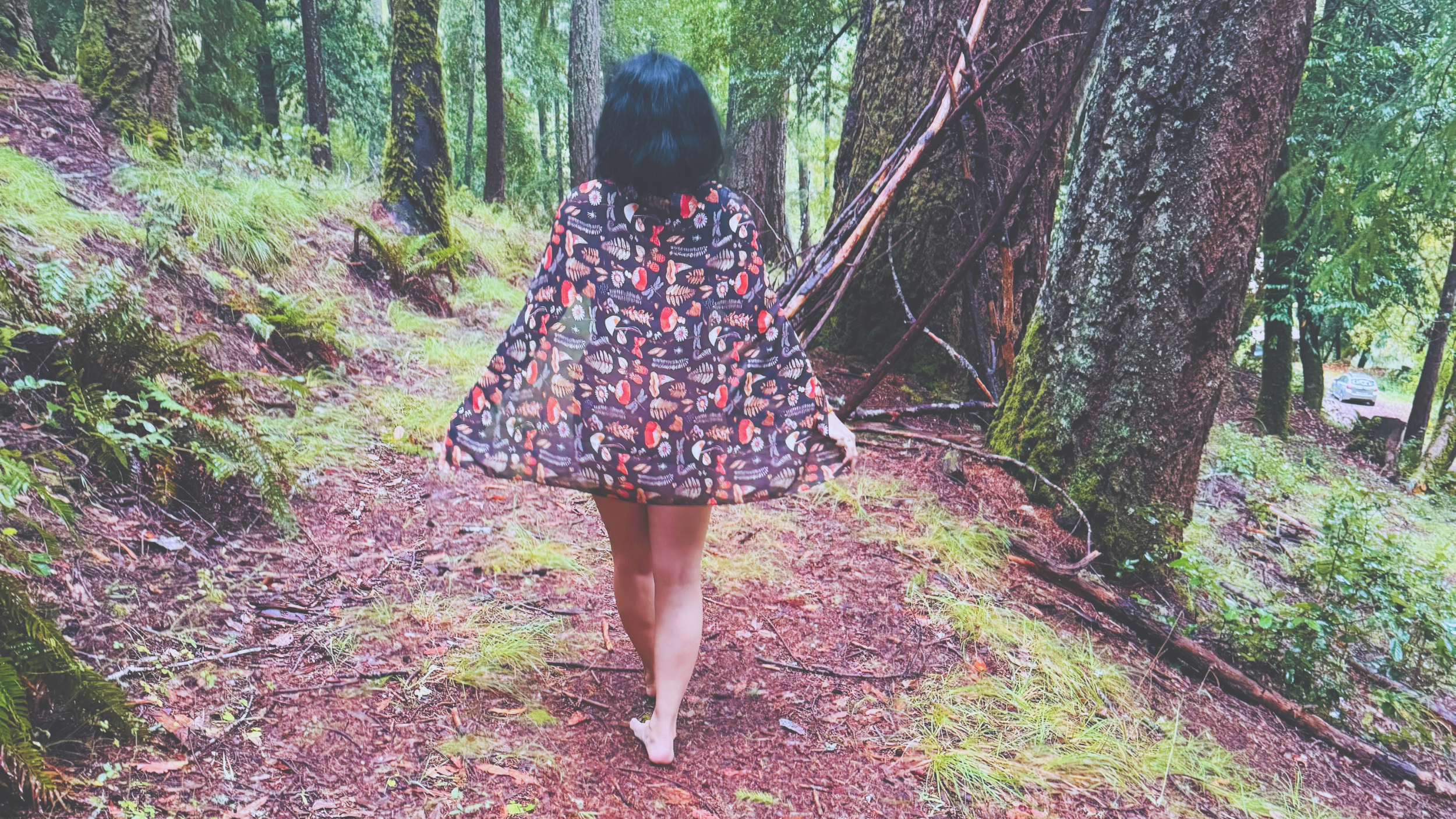 A person walking barefoot on a forest trail lined with trees and ferns, wearing a short dress with butterfly prints.