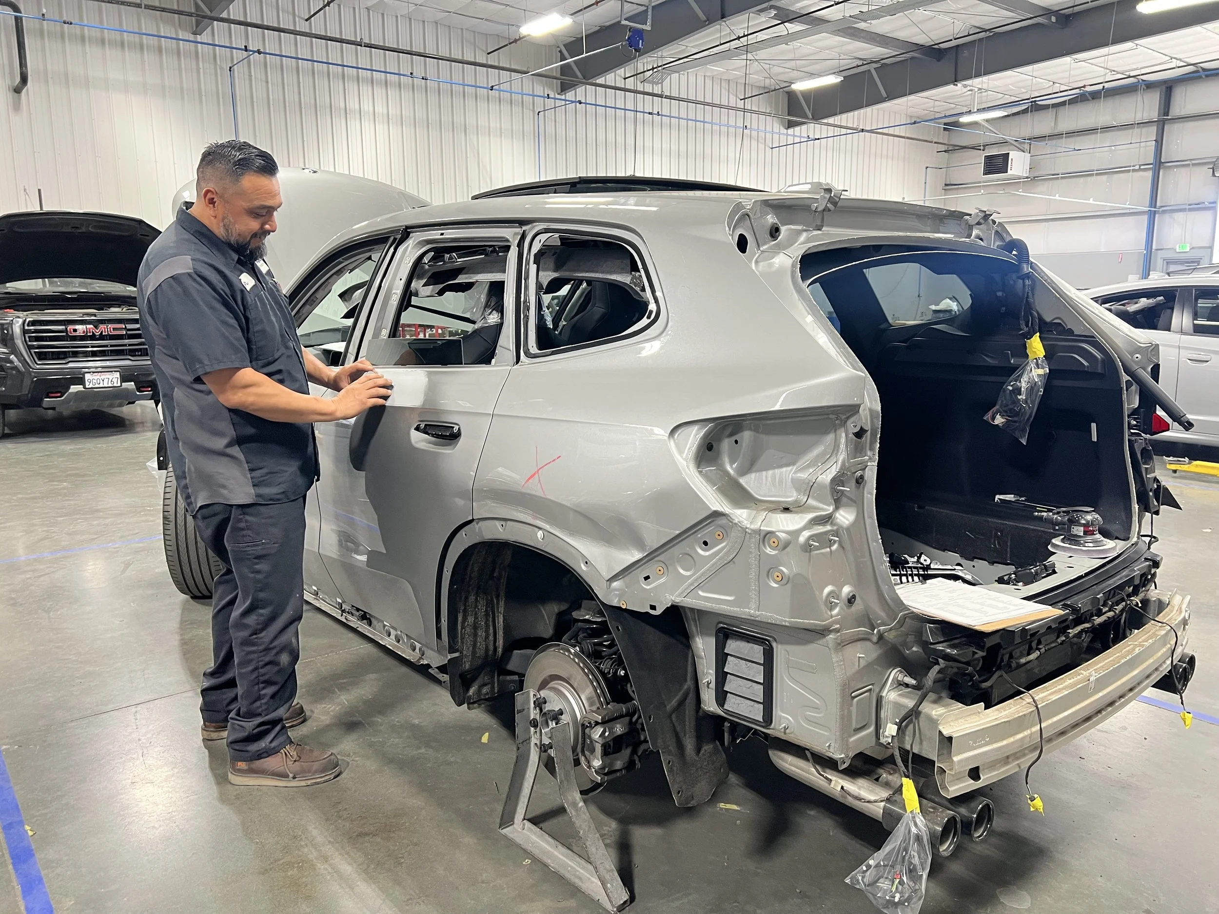 A mechanic working on the stripped down body of a silver SUV in an automotive workshop.