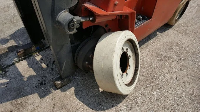 Close-up of a forklift's front wheel with a white solid tire on an industrial asphalt surface.