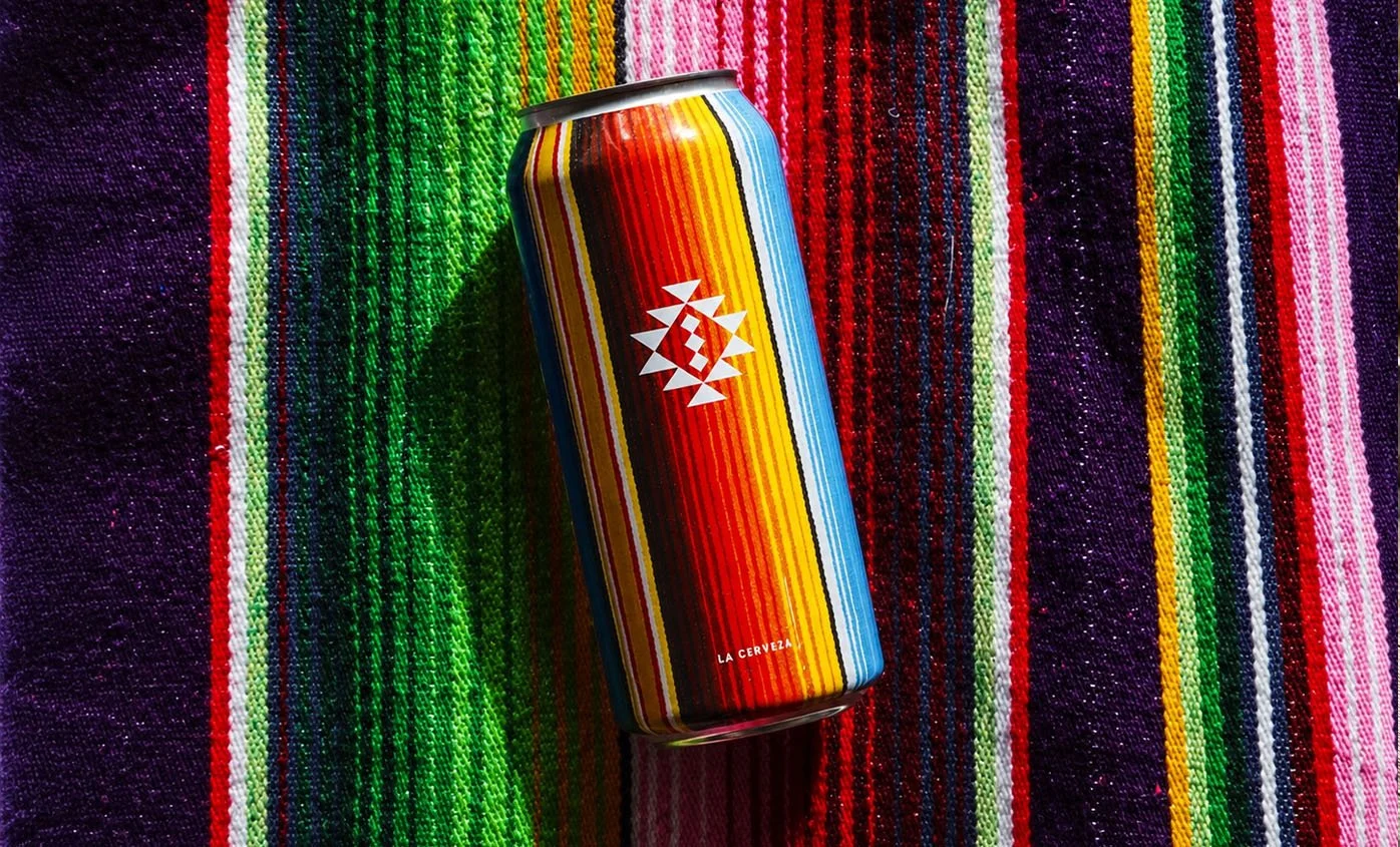 A colorful can with rainbow vertical stripes and a white geometric sun design on a multicolor textured woven blanket.