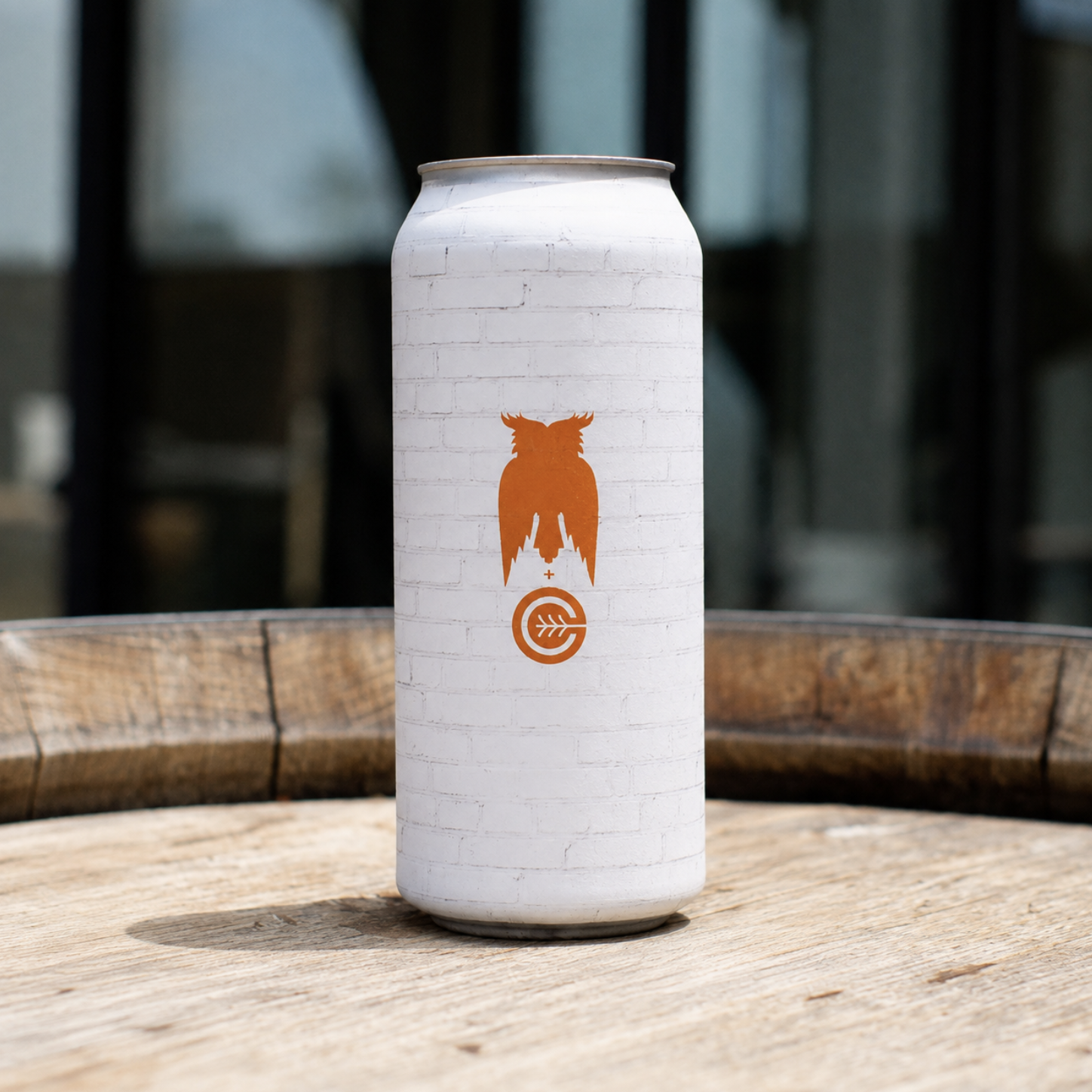 A white aluminum can with an orange silhouette of an owl above a circular logo with a leaf in the center, sitting on a wooden surface.