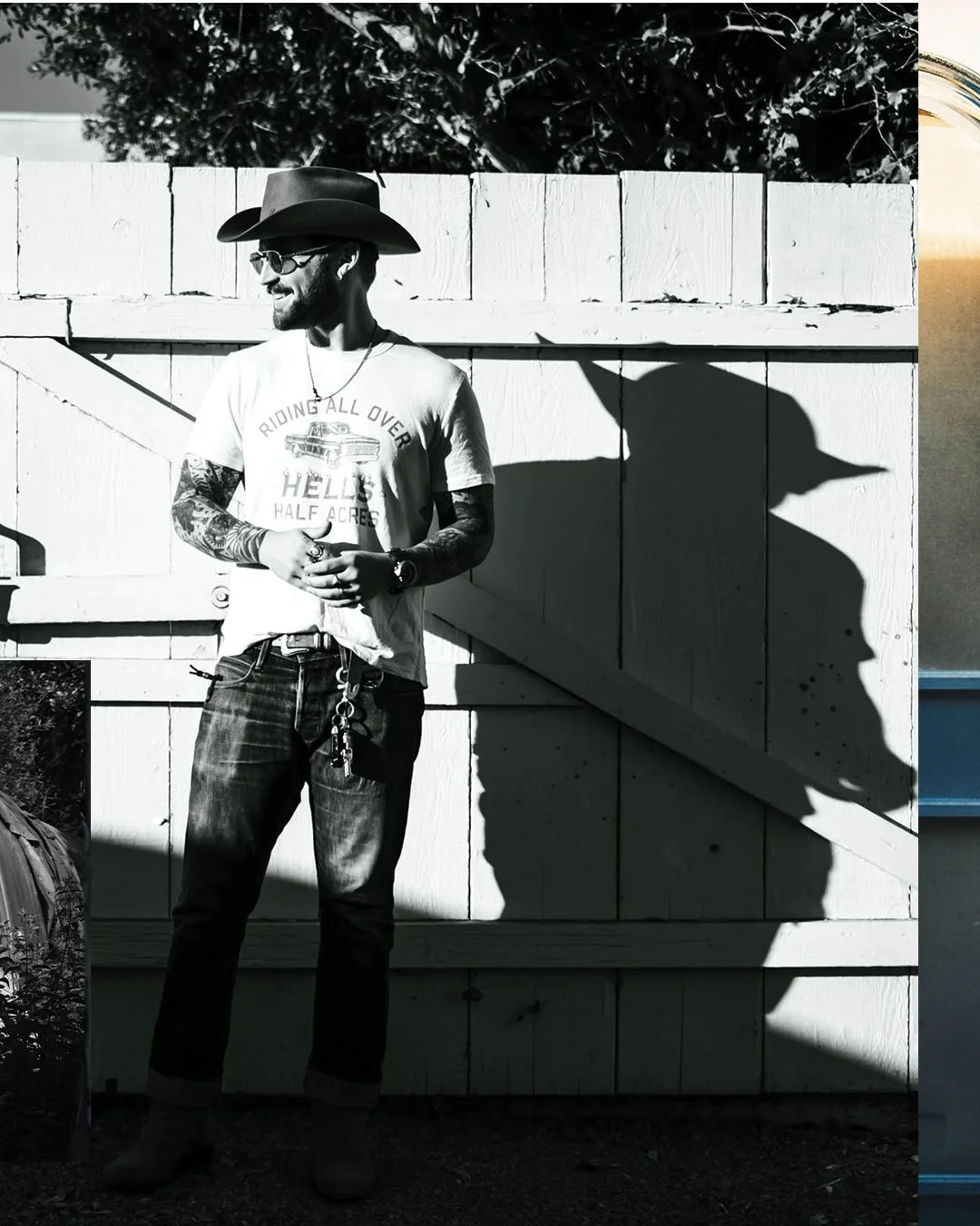 Black and white photo of a man wearing a cowboy hat, sunglasses, a graphic T-shirt, jeans, and boots, standing outside against a wooden fence. His shadow on the fence resembles a dragon or dinosaur head.