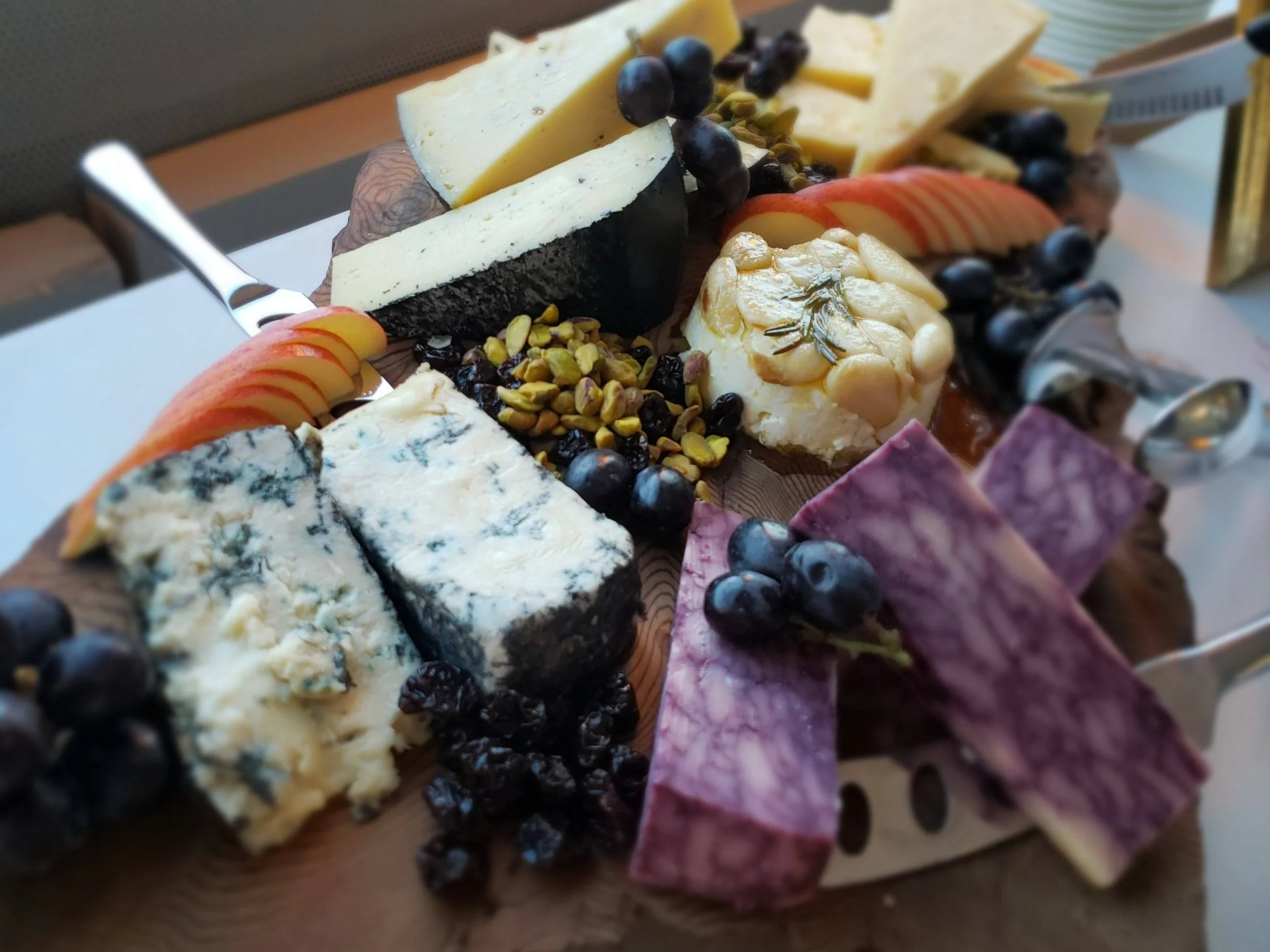 Cheese platter with various cheeses, grapes, sliced apples, nuts, and dried fruits.