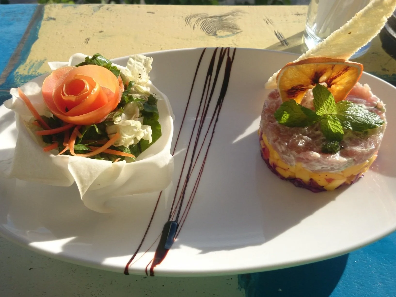 Gourmet salad and tuna tartare on a white plate with decorative balsamic drizzle.