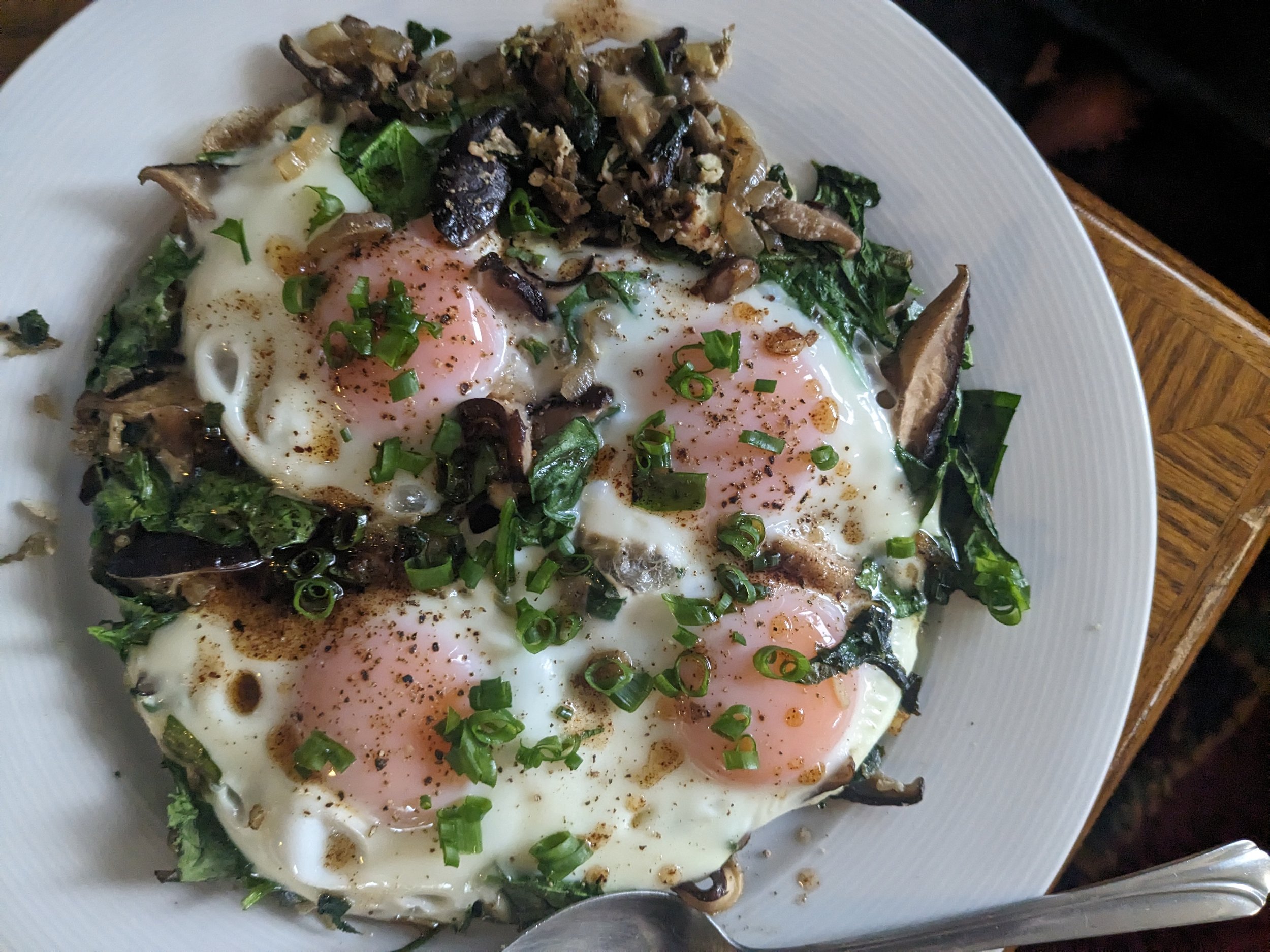 Three poached eggs on sautéed vegetables with herbs on a white plate.