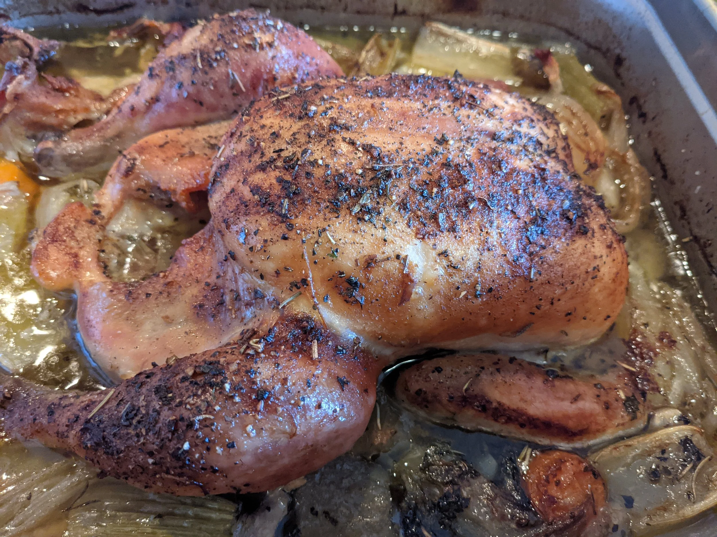 Roasted chicken with herbs in a baking pan with vegetables.