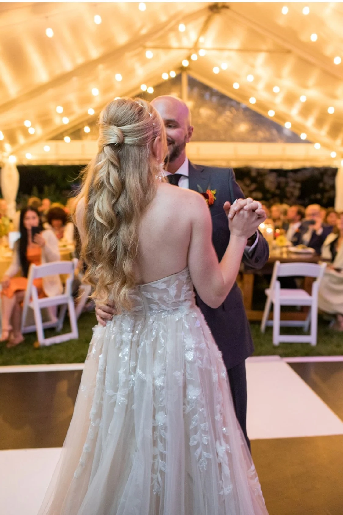 A bride and groom dancing at their wedding reception inside a decorated tent with string lights.