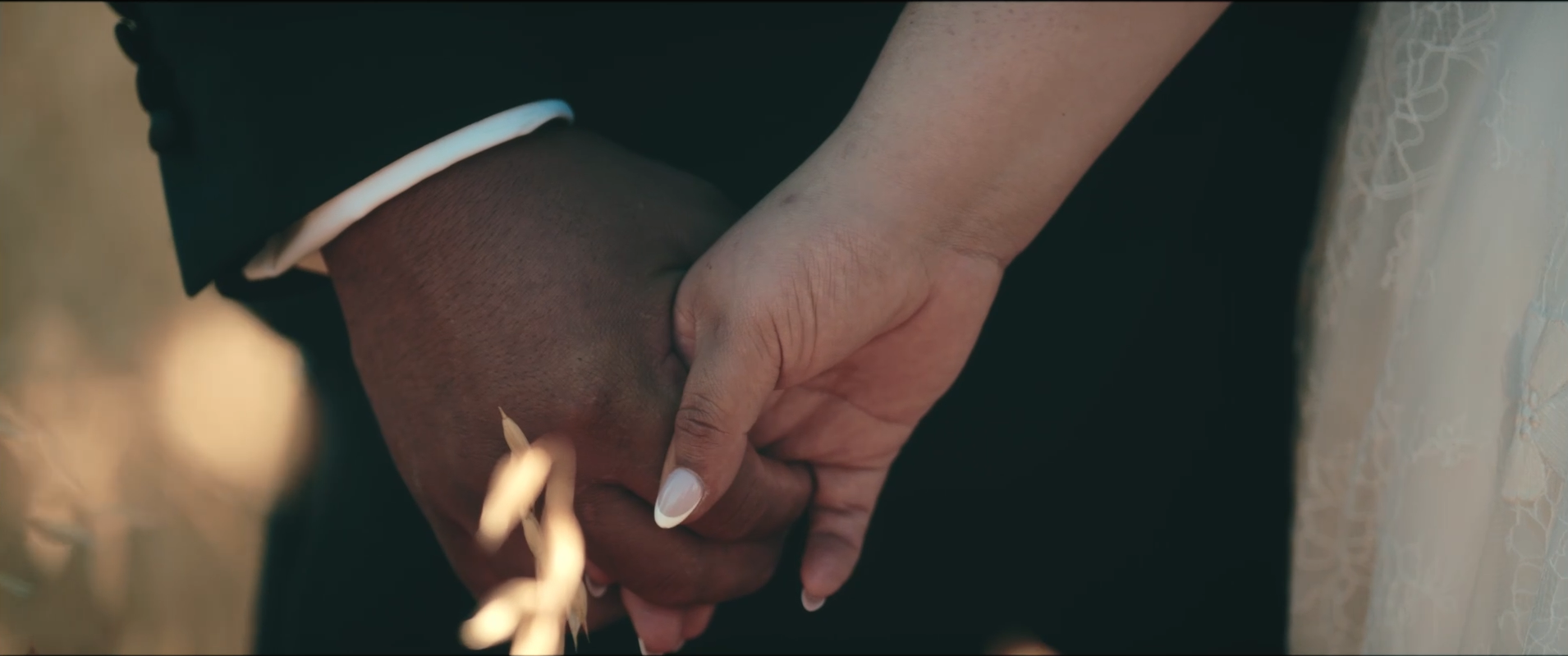 Close-up of a man and woman holding hands, with the woman's finger gently touching the man's hand.