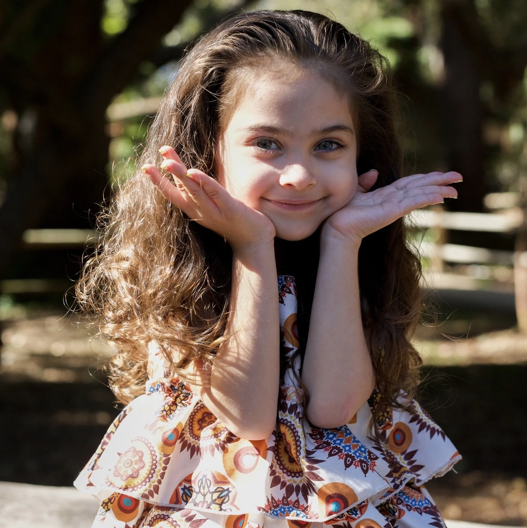 Young girl sits with hands by cheeks, smiling