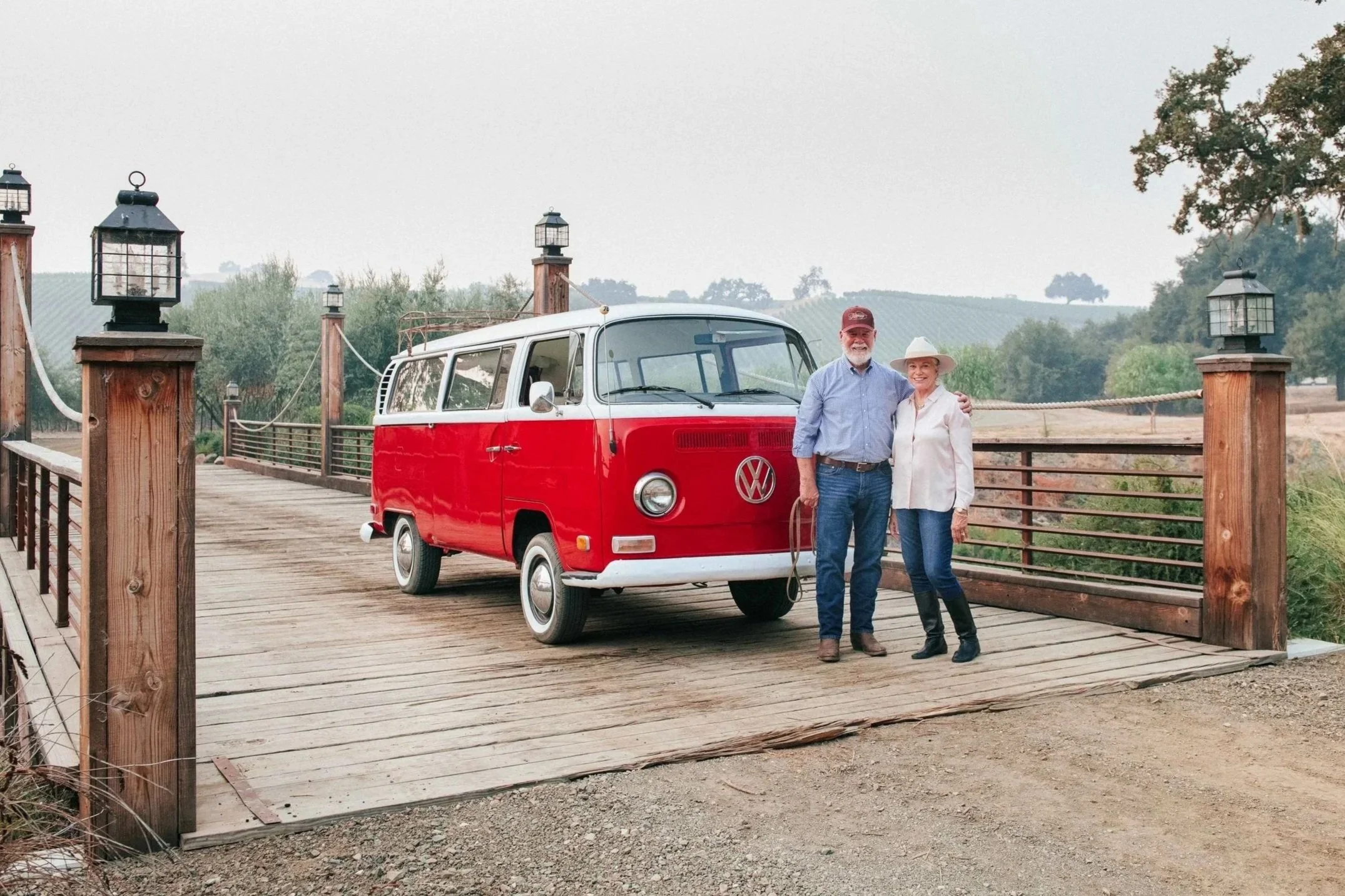 Larry and Sharon Grassini stand in front of a red VW van on the bridge at the Grassini Family Vineyards Estate.