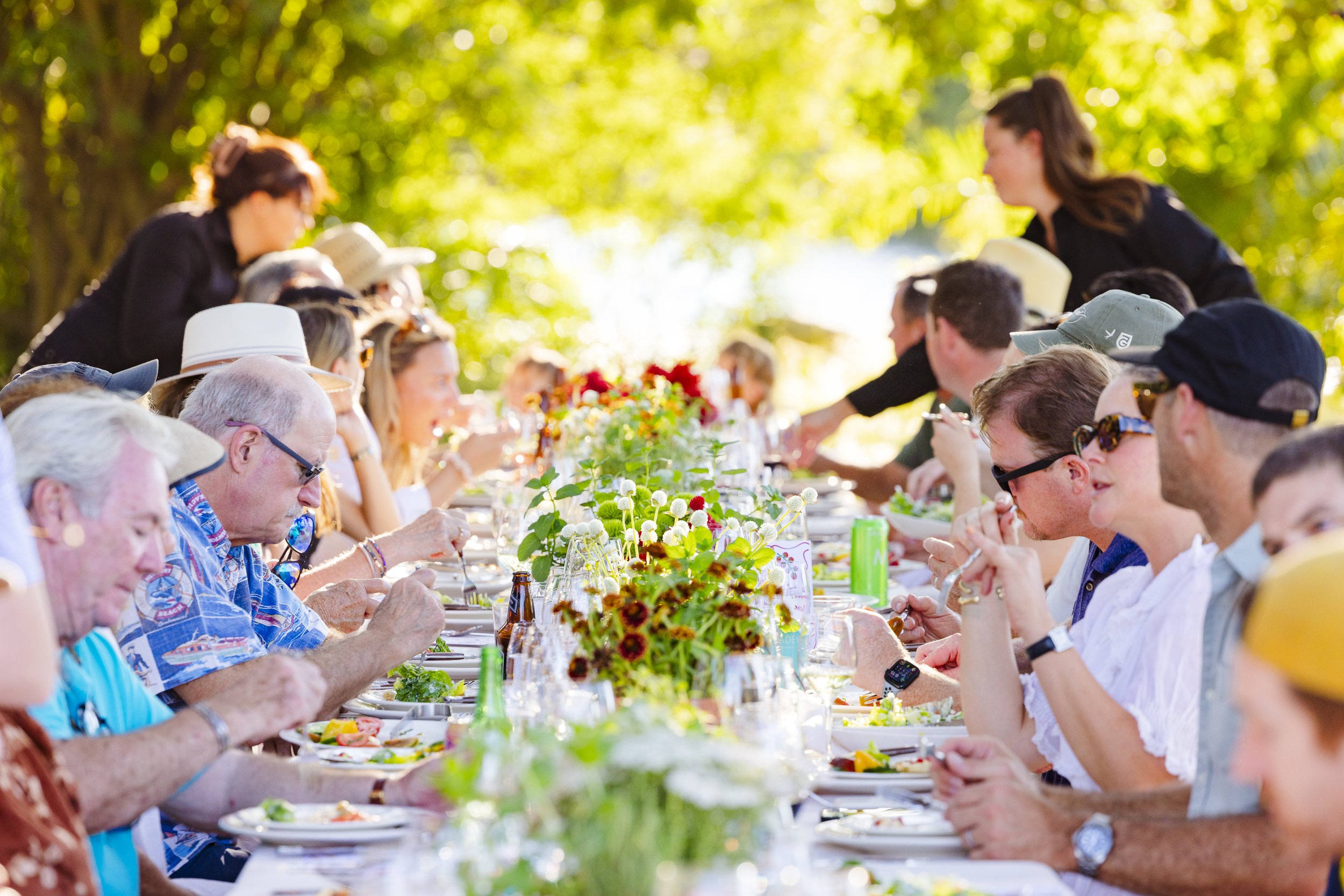 Event guests enjoy a meal, while seated at a long table with seasonal flowers and decor.