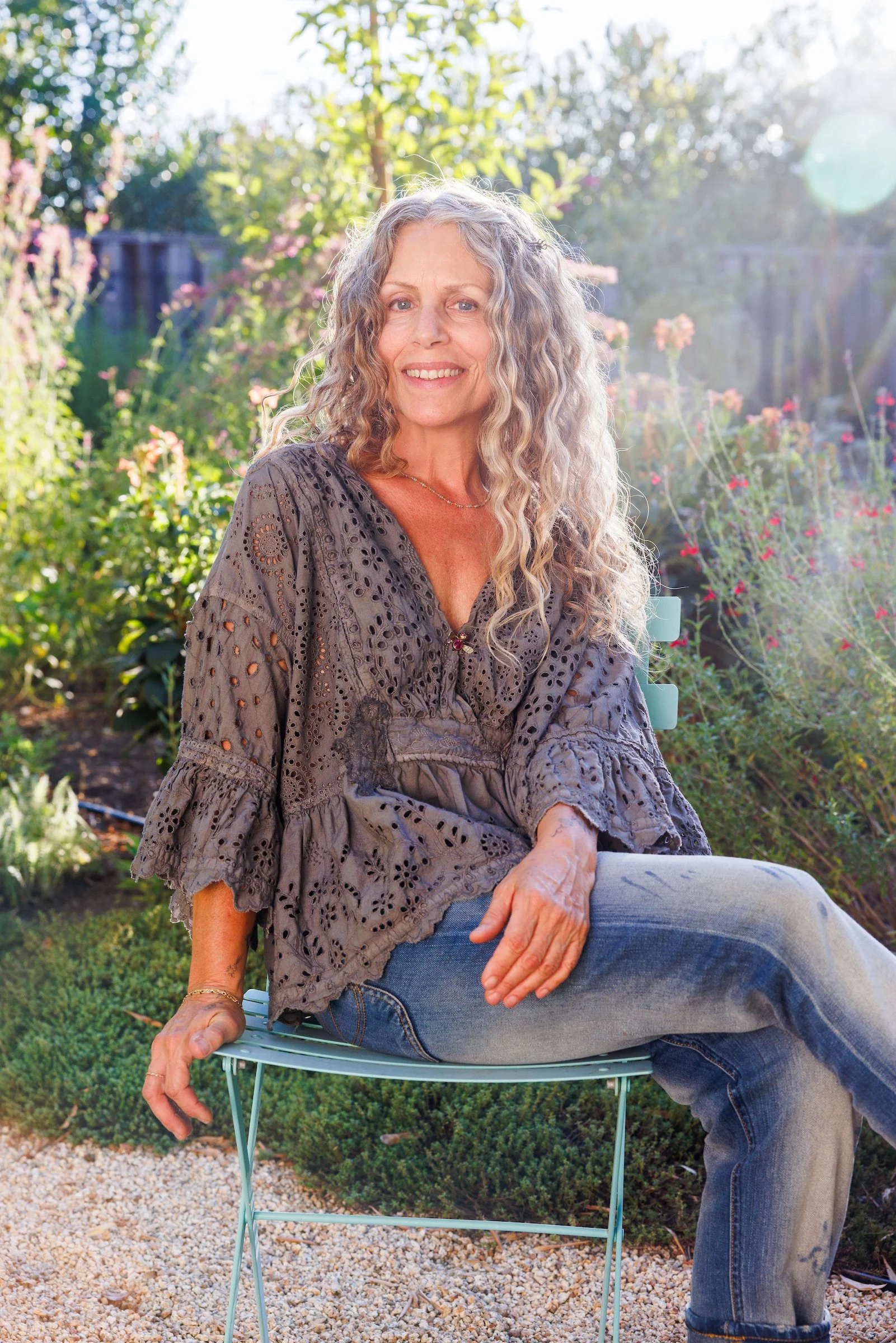 Dina Saalisi, author and speaker sitting on a stool in her garden in St. Helena, CA