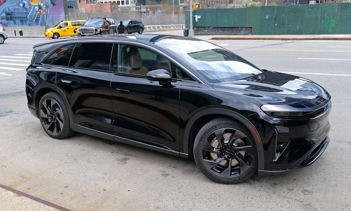 A black Lucid Gravity electric SUV parked on the side of a city street with other vehicles and pedestrians in the background.