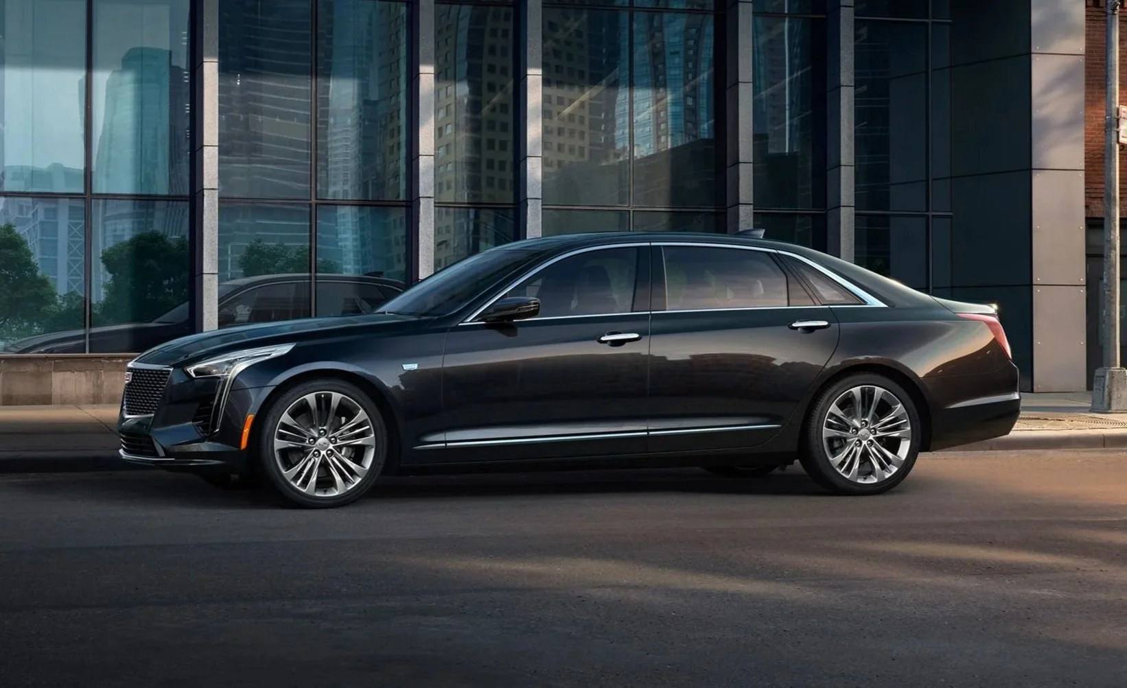 A sleek Cadillac black sedan parked on city street in front of a modern glass building.
