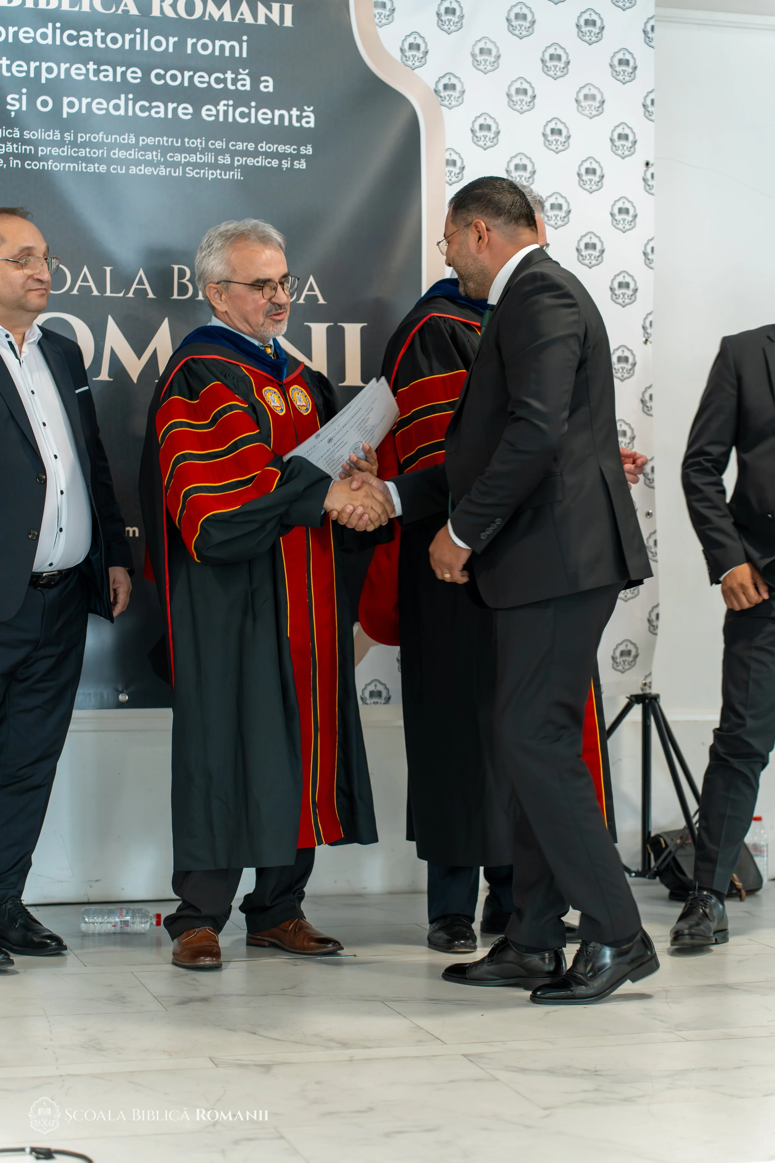 Absolvent felicitat de profesori, cu diploma în mâini.