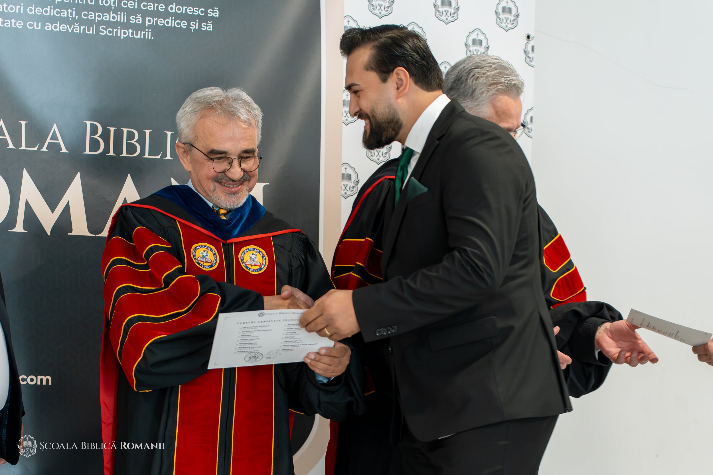 Înmânarea diplomei și felicitări între participanții în robe academice.
