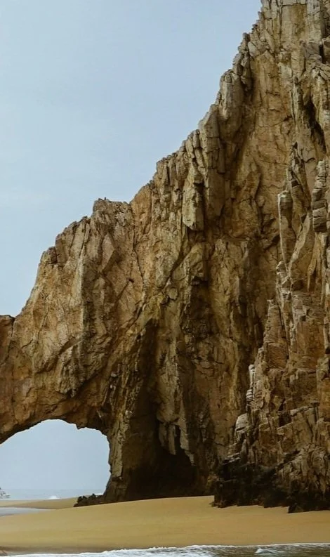 Formaciones rocosas en una playa, con un arco natural y escasa vegetación.