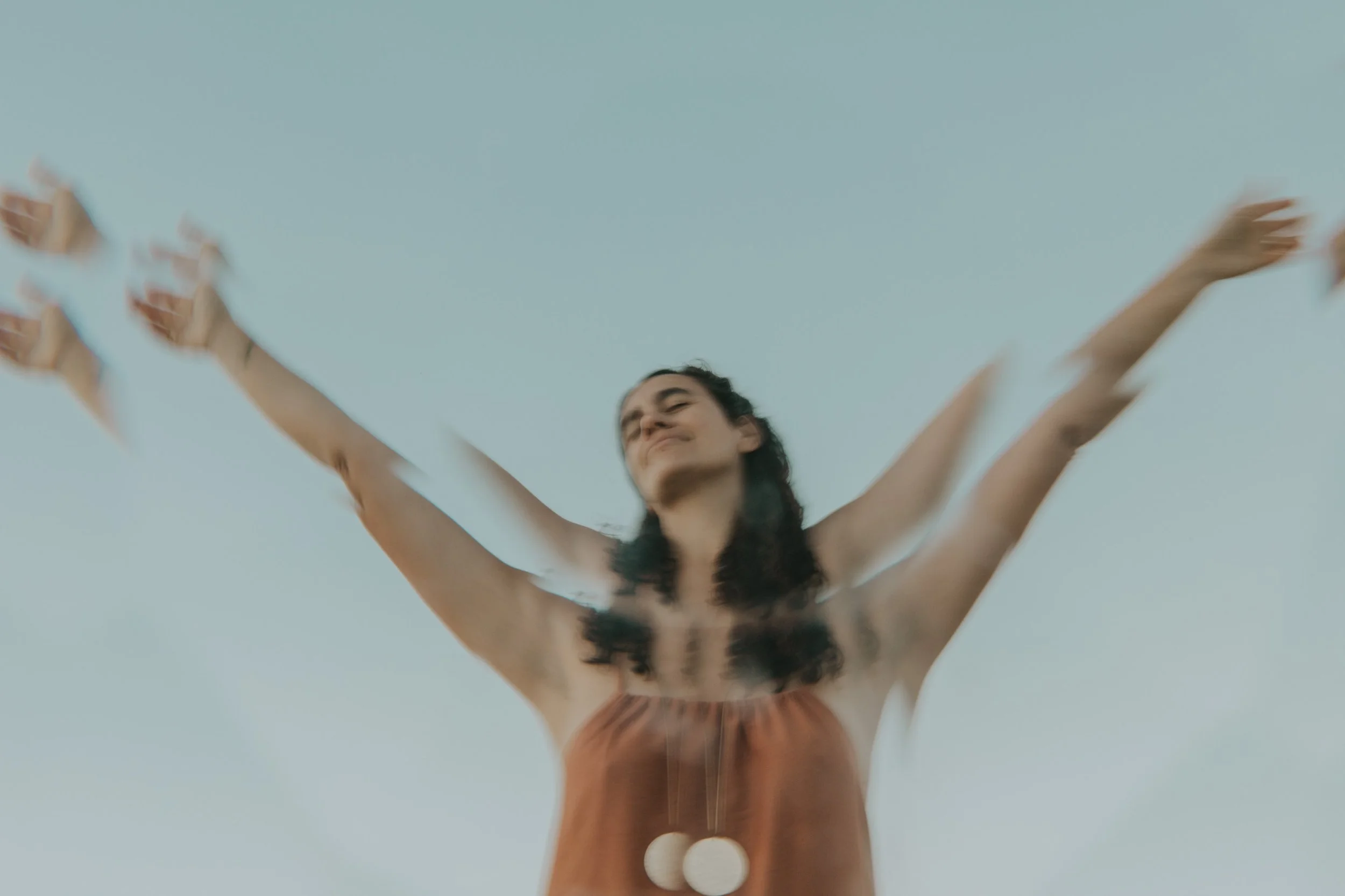 Mujer sonriendo con los brazos abiertos, de espaldas, vistiendo un vestido naranja y rodeada de un cielo despejado.