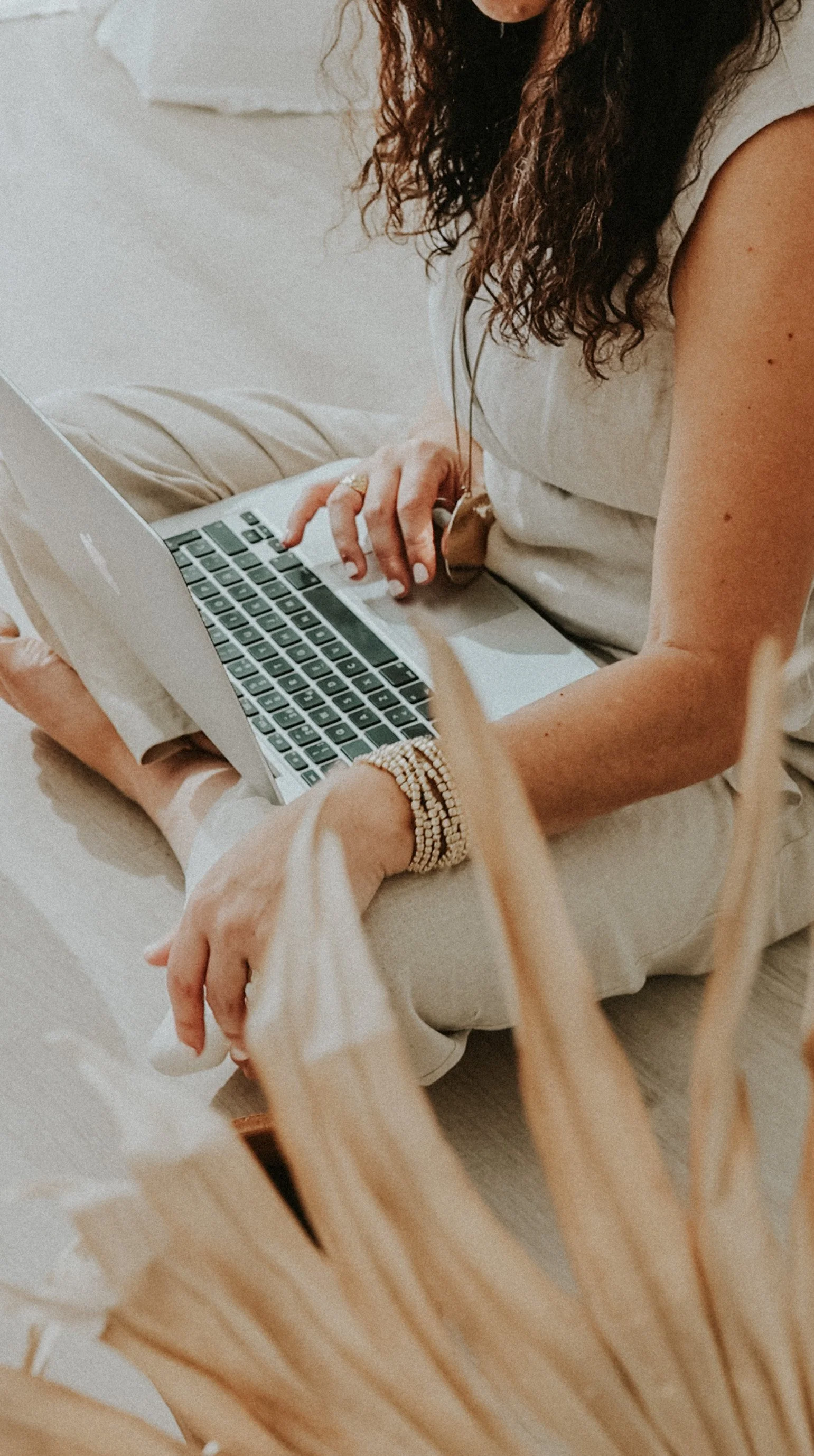 Persona usando una computadora portátil en un espacio interior, con cabello rizado y accesorios de pulseras y anillos.