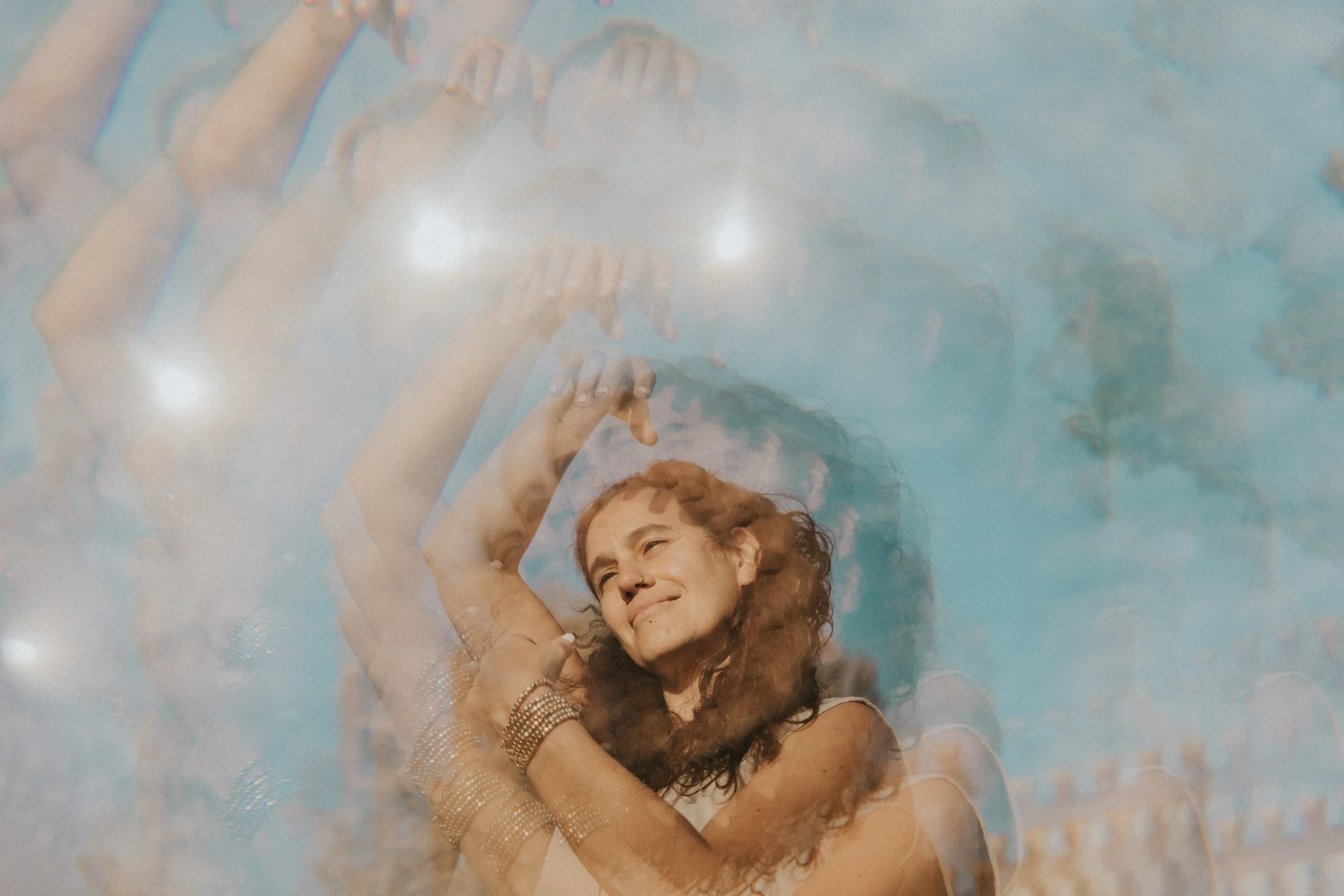 Mujer con cabello rizado y sonrisa, con múltiples brazos extendidos hacia arriba, en un fondo de cielo azul y nubes.