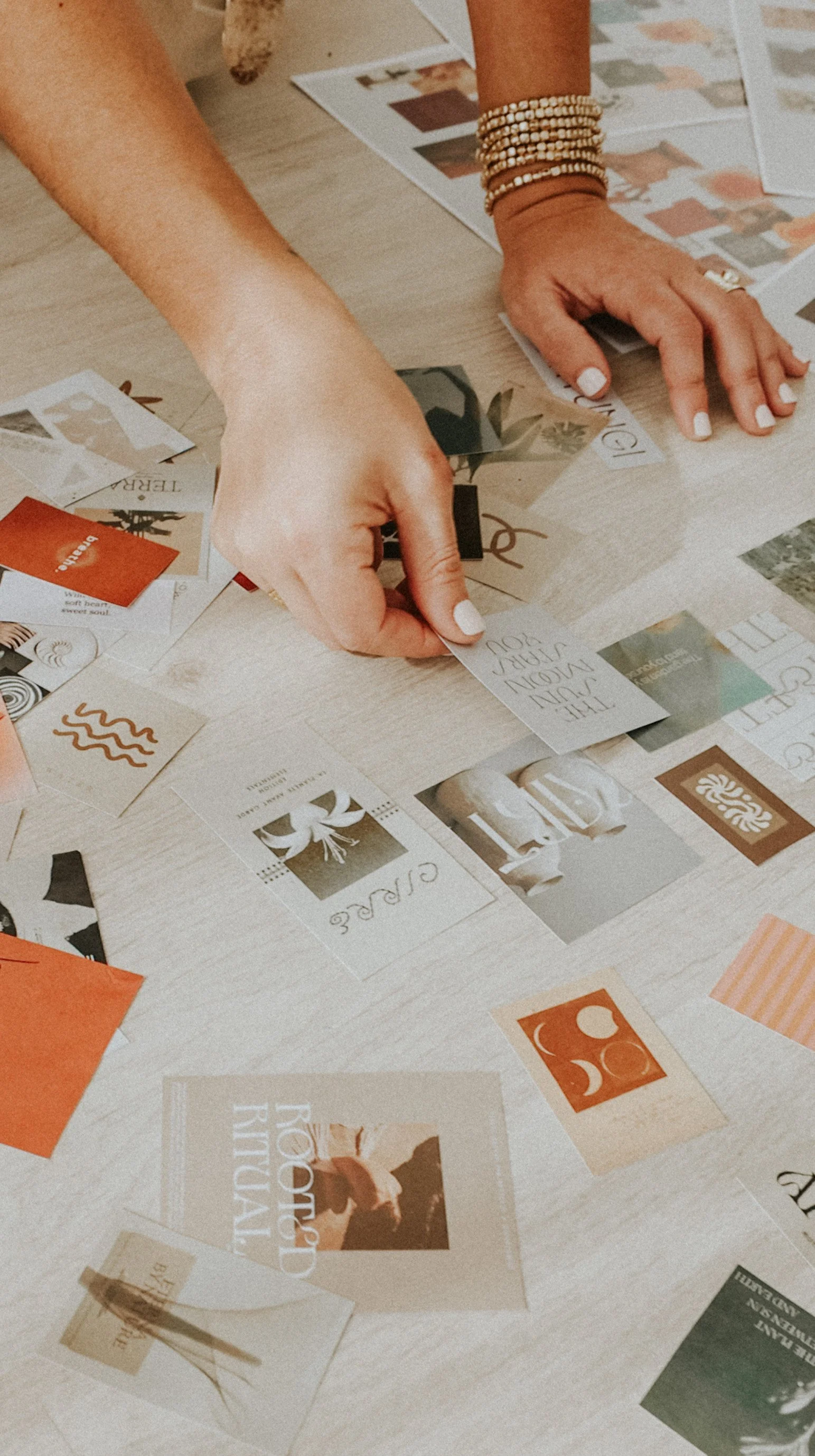 Manos organizando tarjetas y fotos sobre una mesa de color claro.