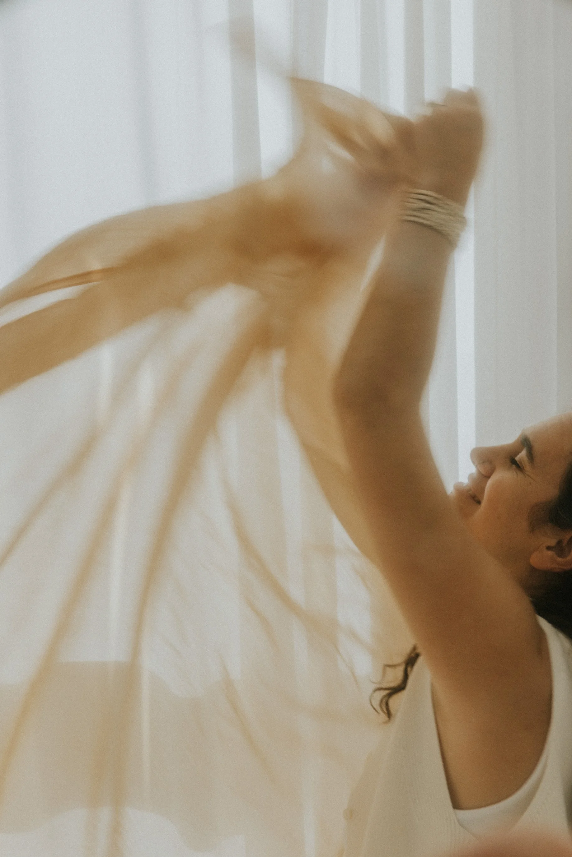 Una mujer sonriente juega con su gato naranja en una habitación iluminada por luz natural.