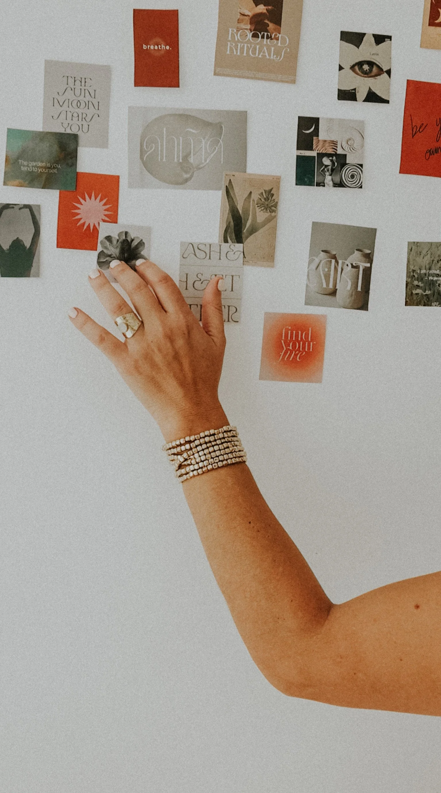 Mano adornada con pulseras y anillo tocando notas adhesivas con frases y diseños en una pared blanca.