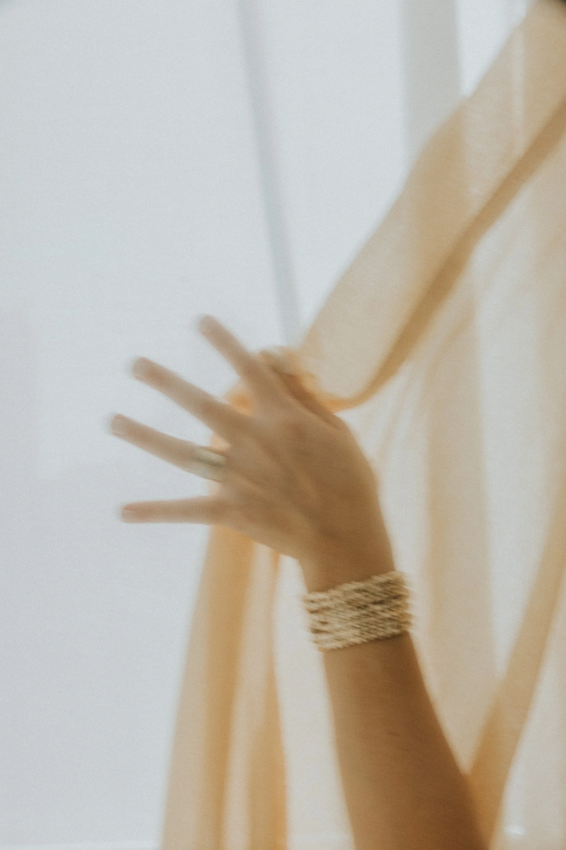 Una mano con pulsera dorada tocando una estructura en colores beige y blanco.