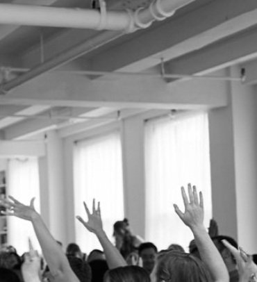 A group of people raising their hands in a room with large windows and white walls.