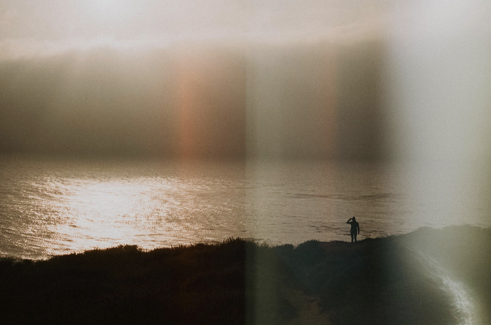 A person standing on a hill overlooking the ocean at sunset.