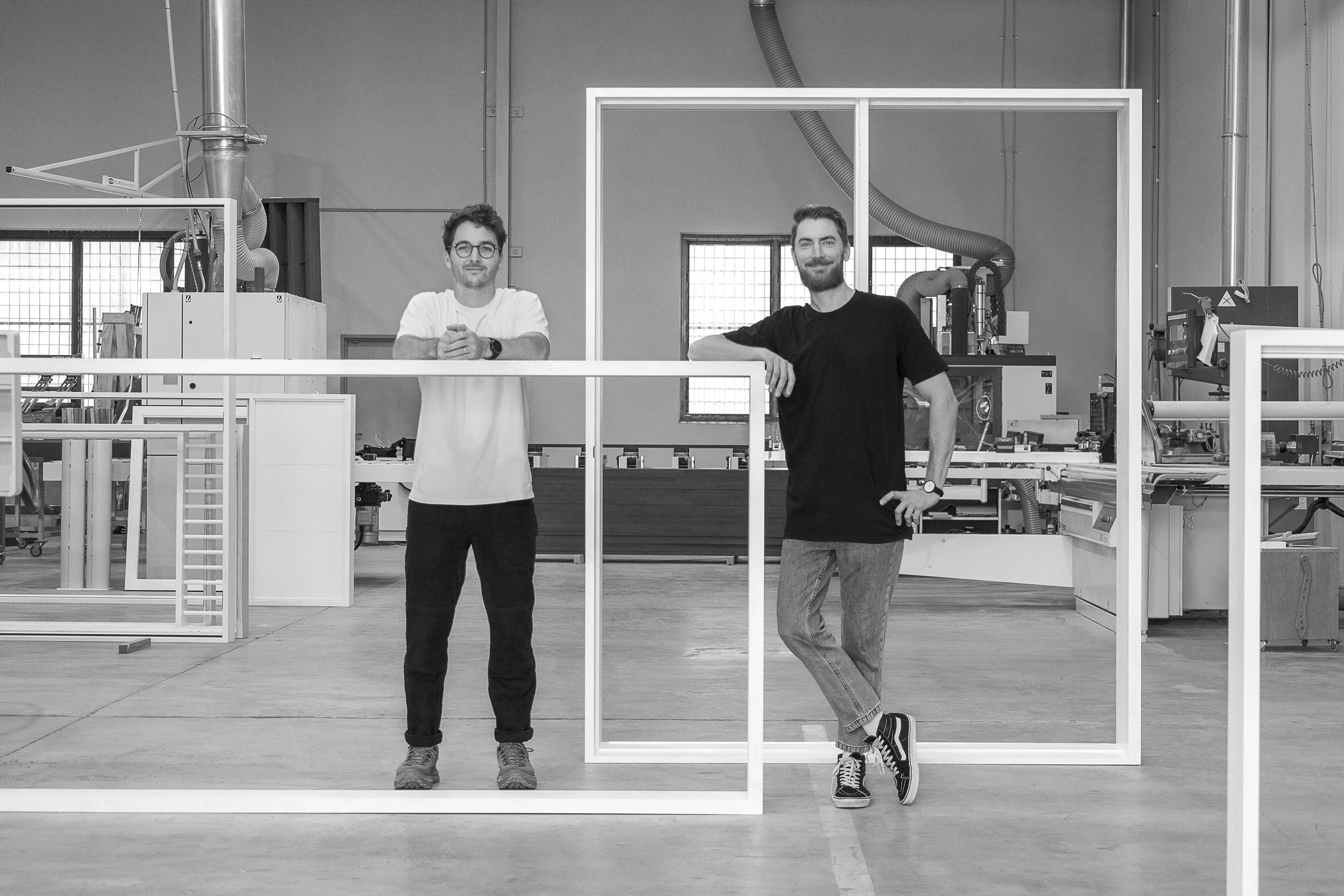 Founders of Aperture Joinery in their Brisbane workshop, standing among timber window and door frames.
