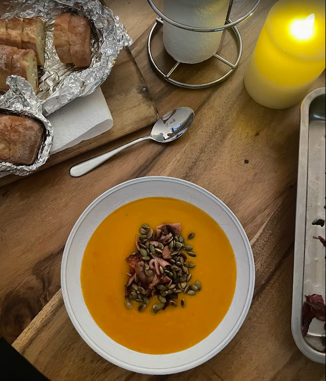 A bowl of homemade pumpkin soup with crusty bread and a candle on a wooden table
